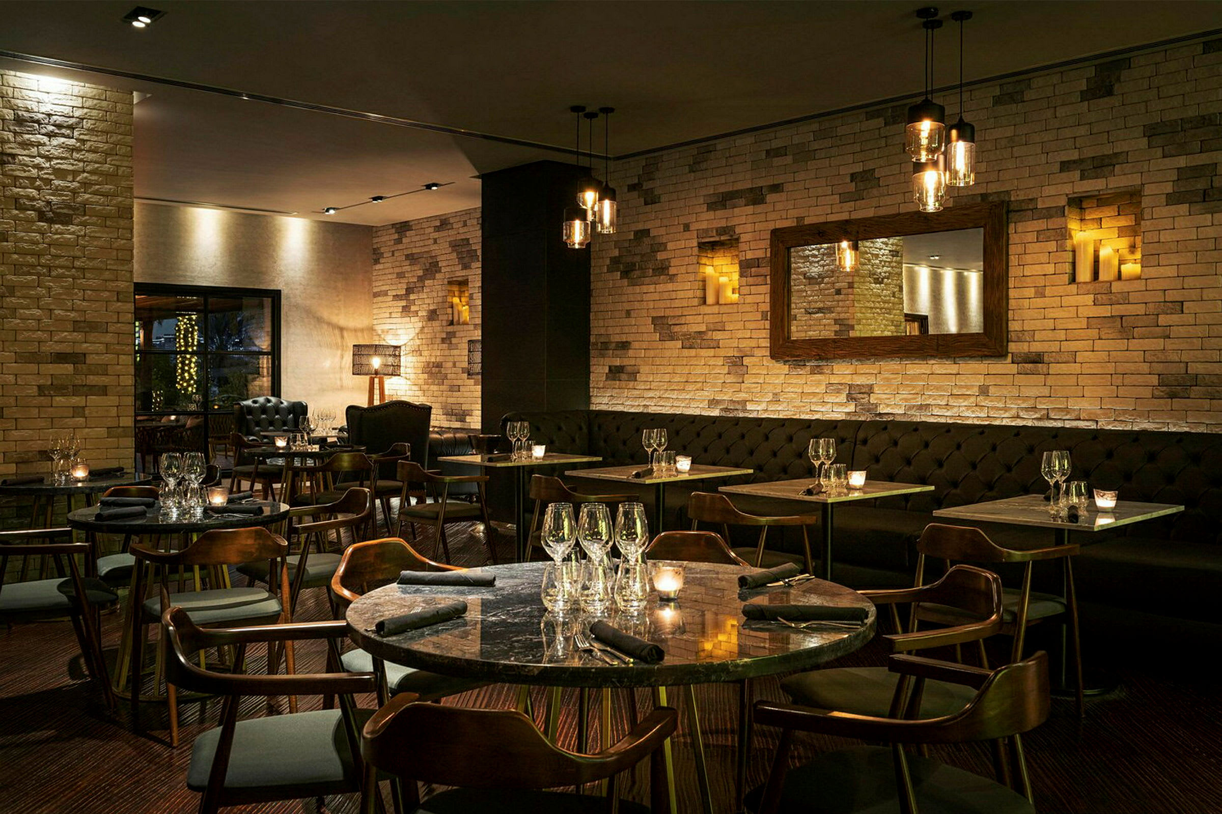 En stilren restaurang med tegelväggar, mörka möbler och belysning skapar en mysig atmosfär. (AI-genererad text)