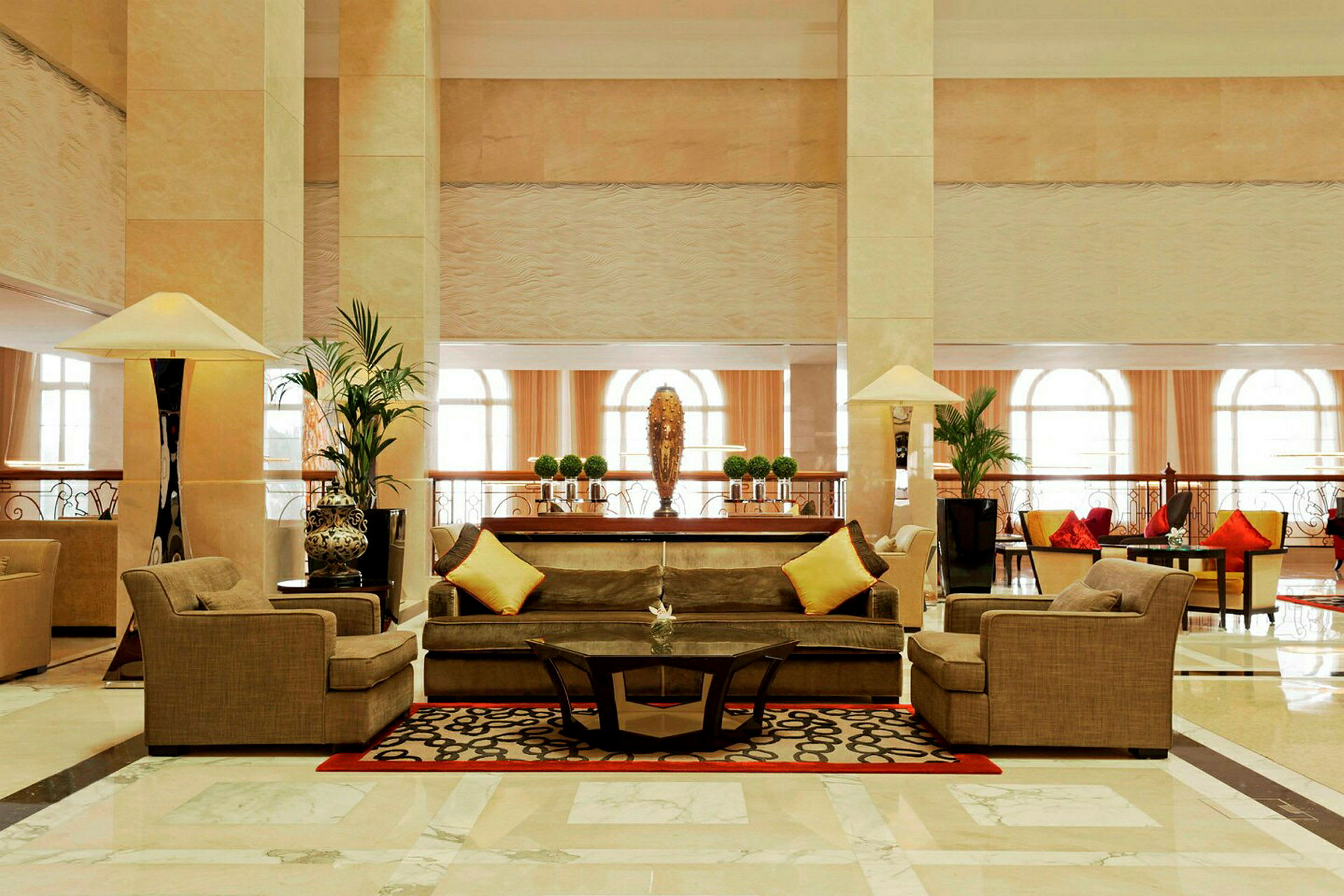 Elegant hotellobby med beige soffor och gula kuddar samt ett glasbord på en dekorativ matta. (AI-genererad text)