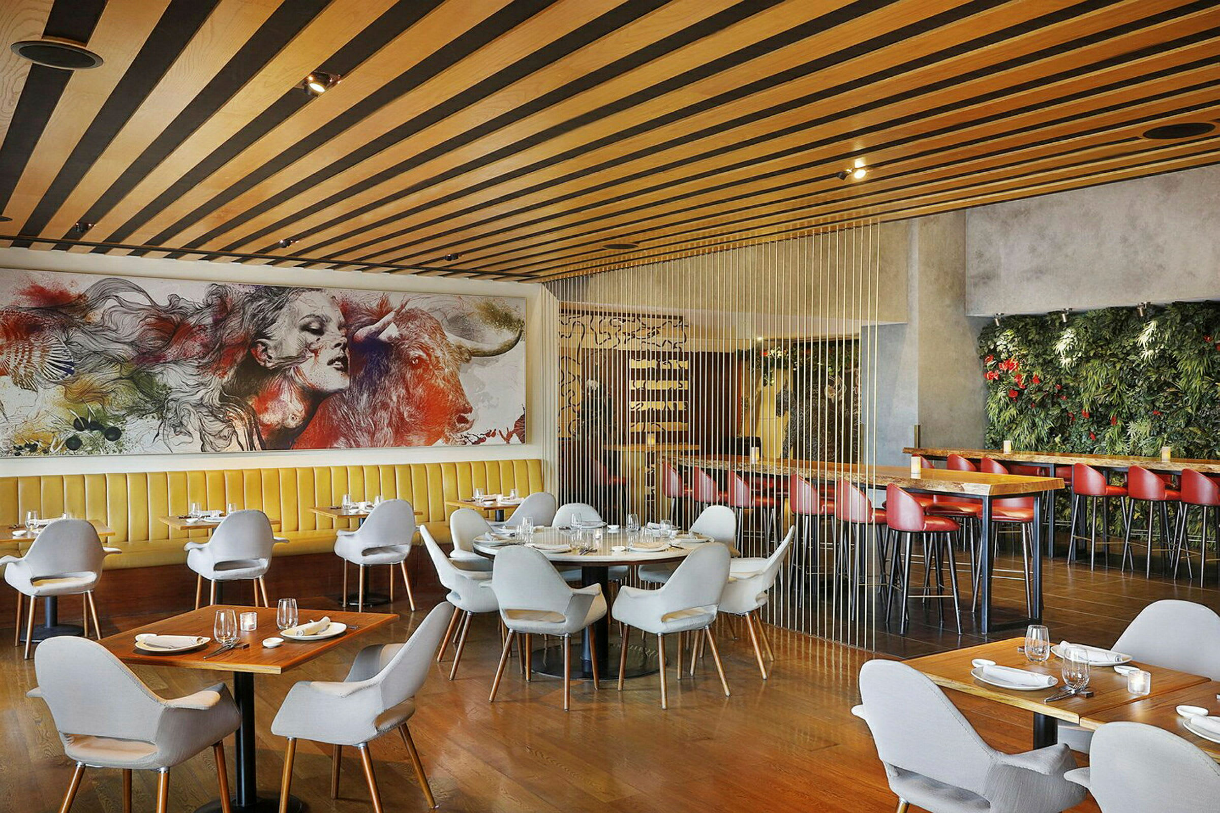 Interiör av en modern restaurang med eleganta stolar och bord, en stor målning på väggen och växtbaserad dekoration. (AI-genererad text)