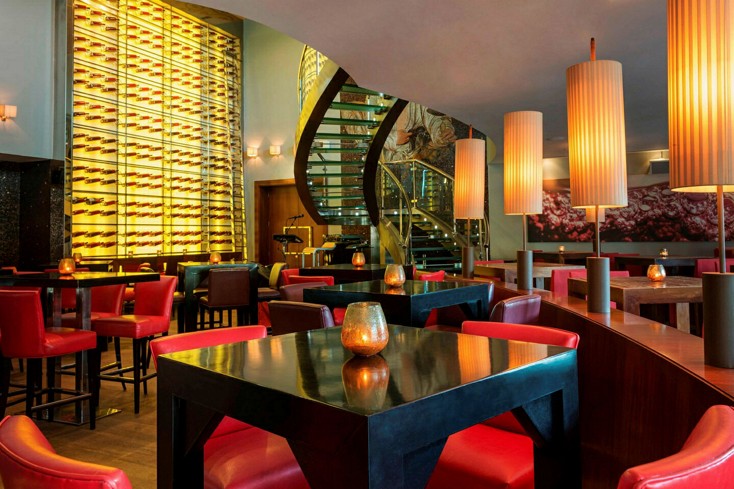 Interiör av en restaurang med moderna möbler och röd dekor, upplyst av stora lampor. (AI-genererad text)