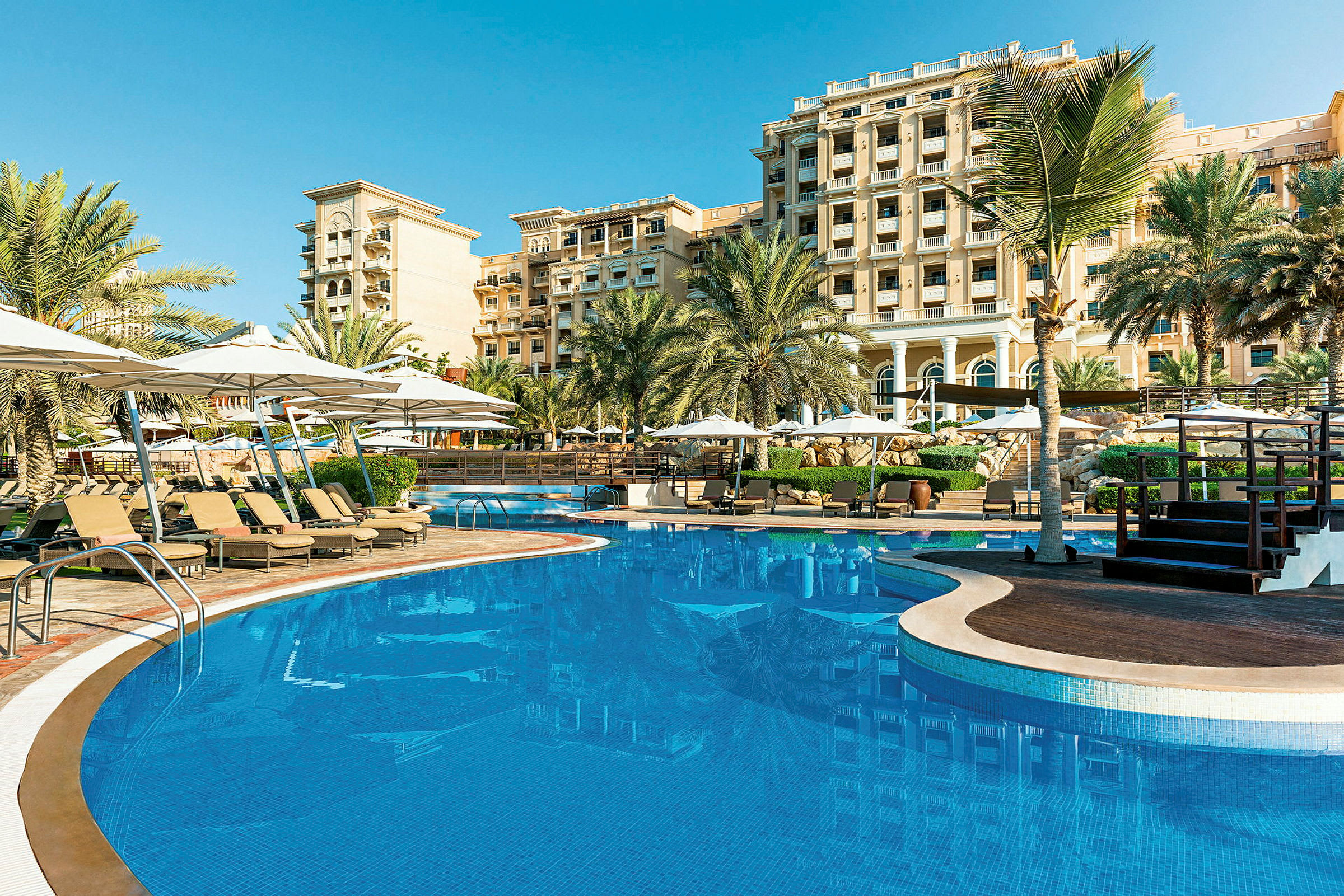 Ett hotellområde med en pool, solstolar och palmer under en klarblå himmel. (AI-genererad text)