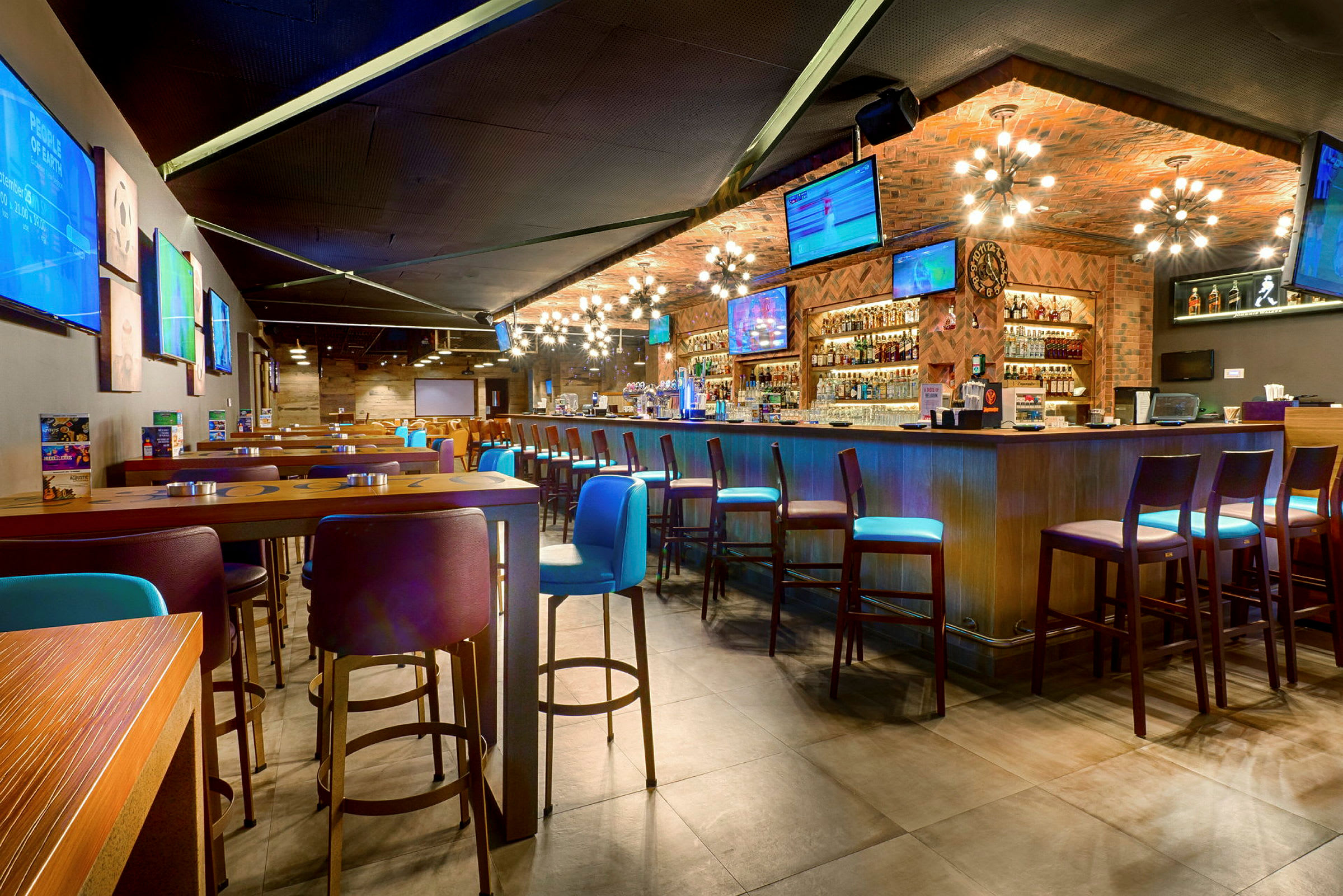 Interiör av en modern bar med höga bord och stolar samt flera TV-skärmar på väggarna. (AI-genererad text)