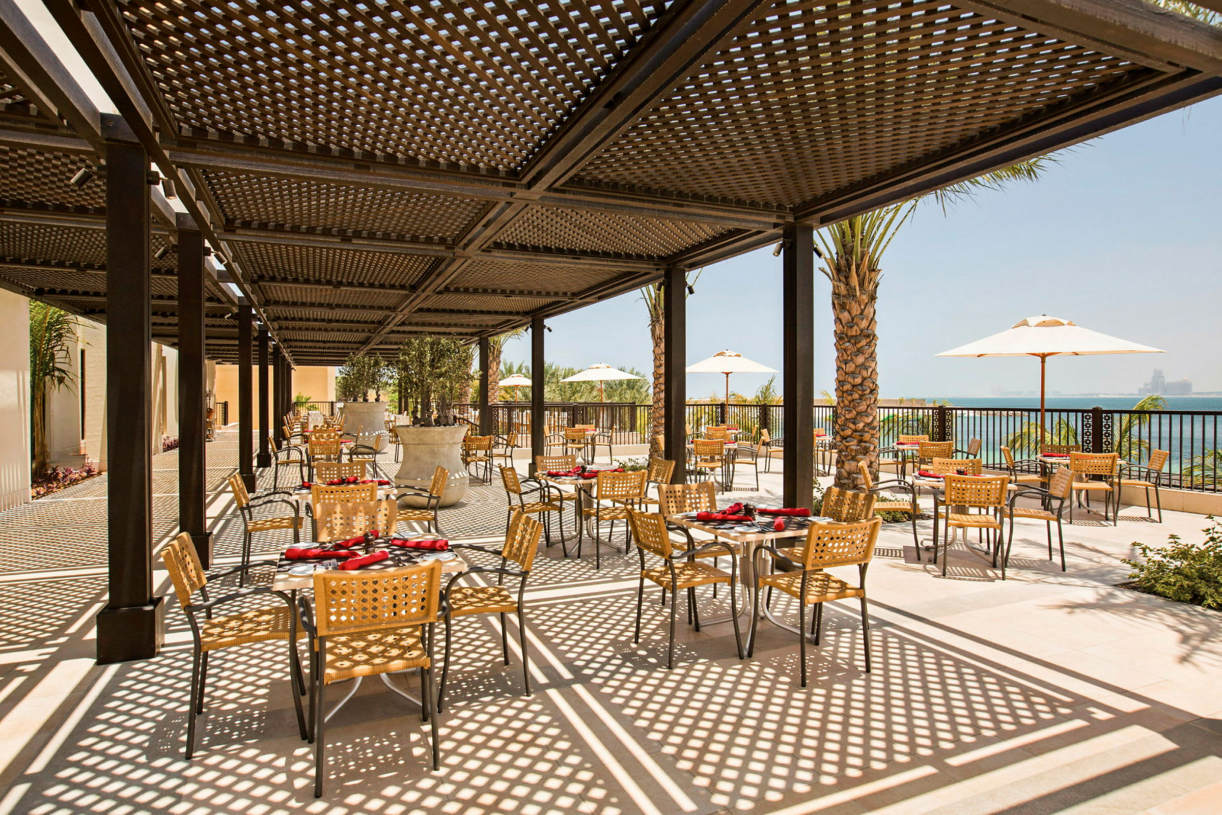 Utomhusrestaurang med bord och stolar under skuggande pergola. (AI-genererad text)