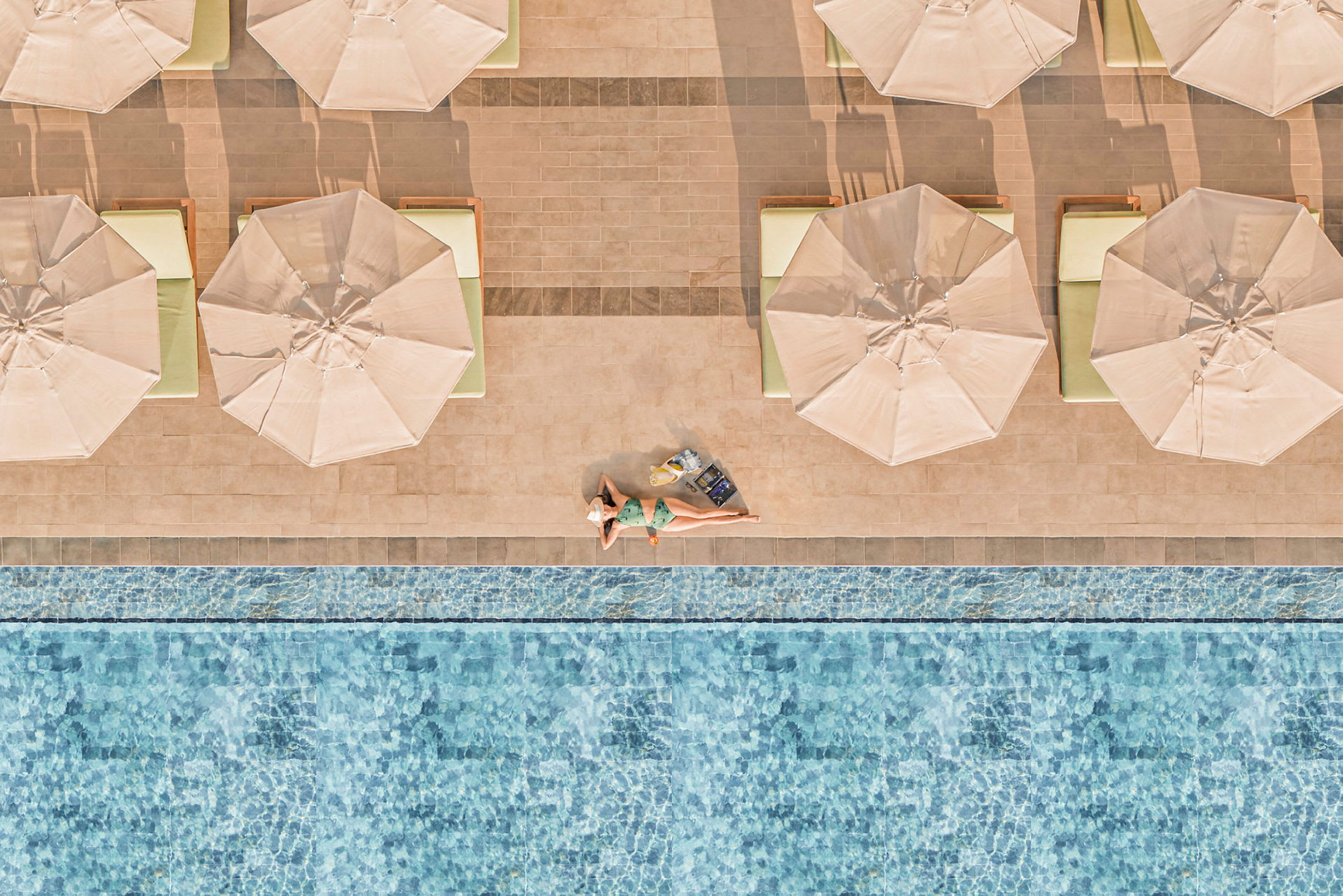 En person ligger och solar på en solstol vid en pool med parasoll och vatten i bakgrunden. (AI-genererad text)