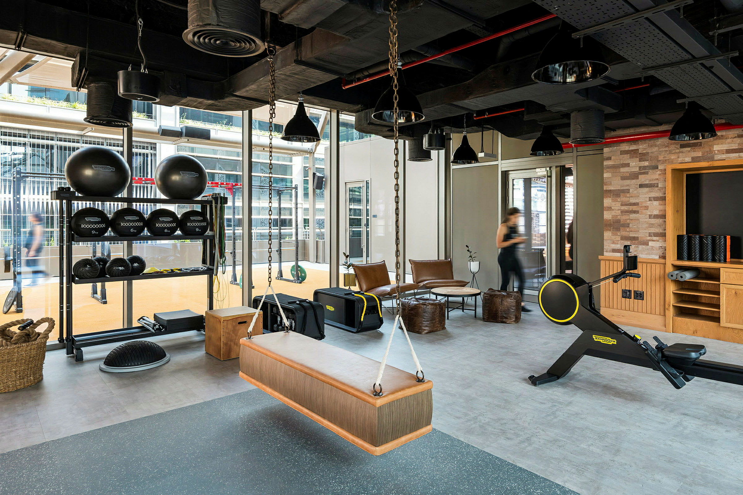 Gym med olika träningsutrustning, sittplatser och stora fönster. (AI-genererad text)