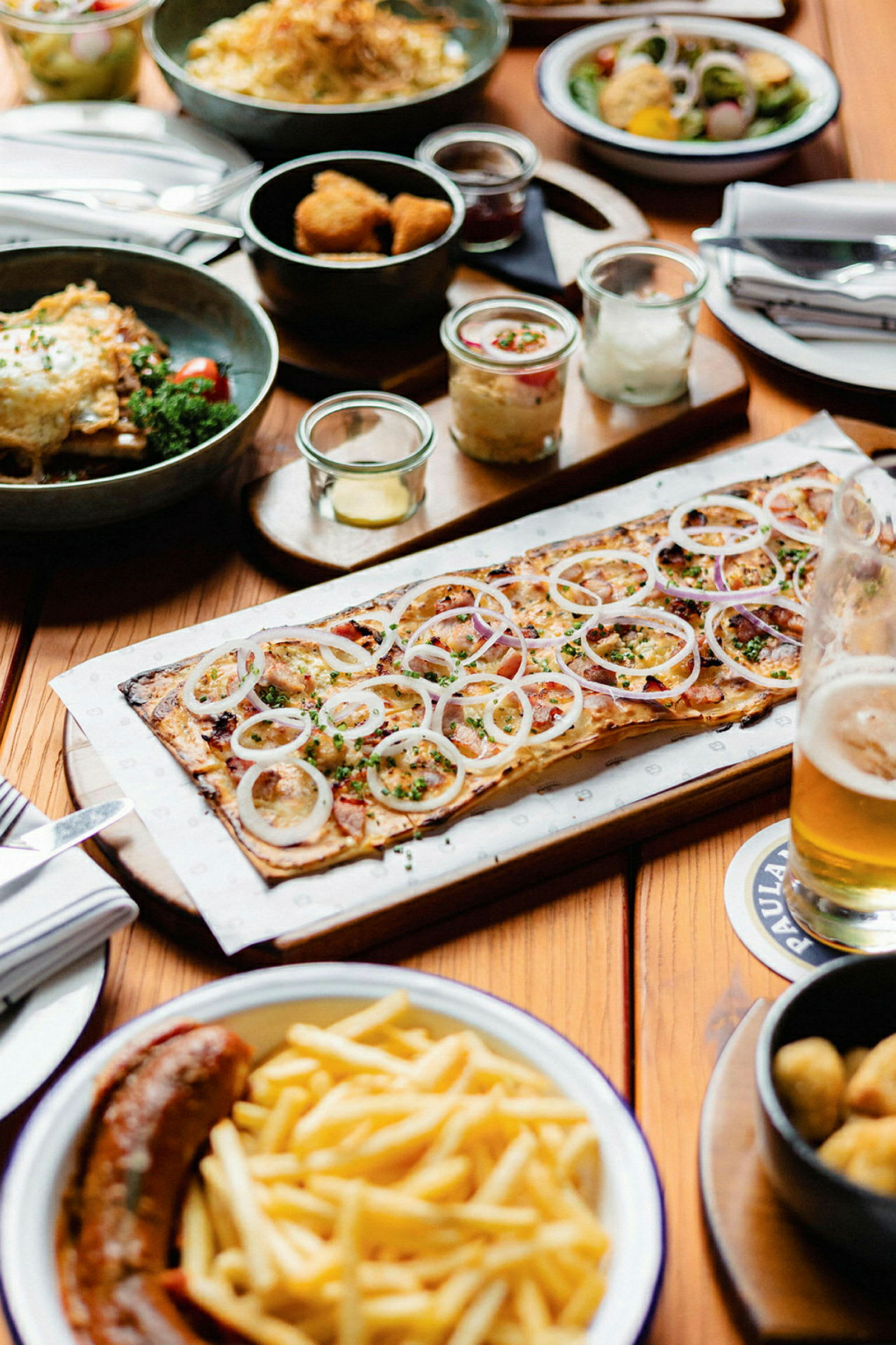 Ett bord dukat med olika maträtter, inklusive en pizza med lök, pommes frites och en korv. (AI-genererad text)