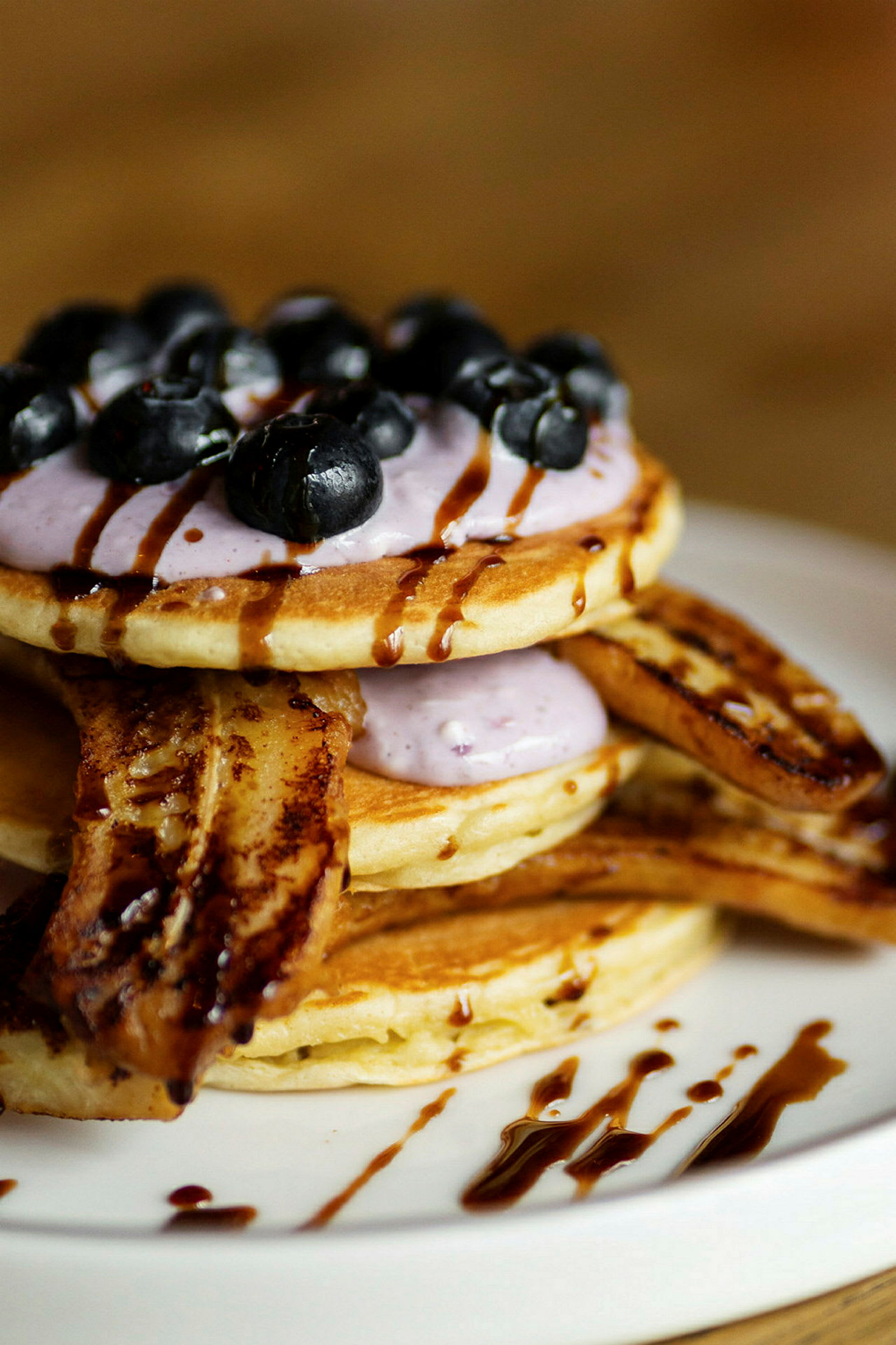 En tallrik med pannkakor toppade med blåbär, sås, och bananskivor. (AI-genererad text)