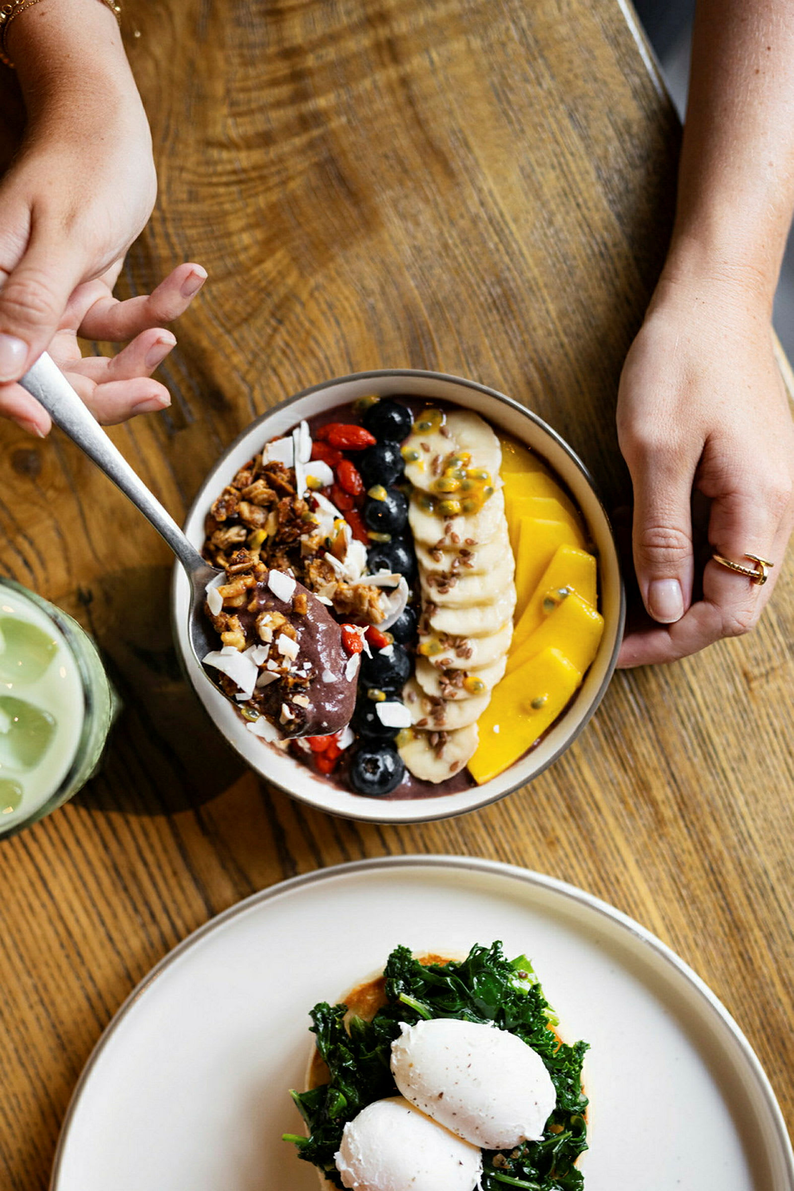 En tallrik med en färgglad acai bowl och en annan med pocherade ägg och grönsaker på ett träbord. (AI-genererad text)