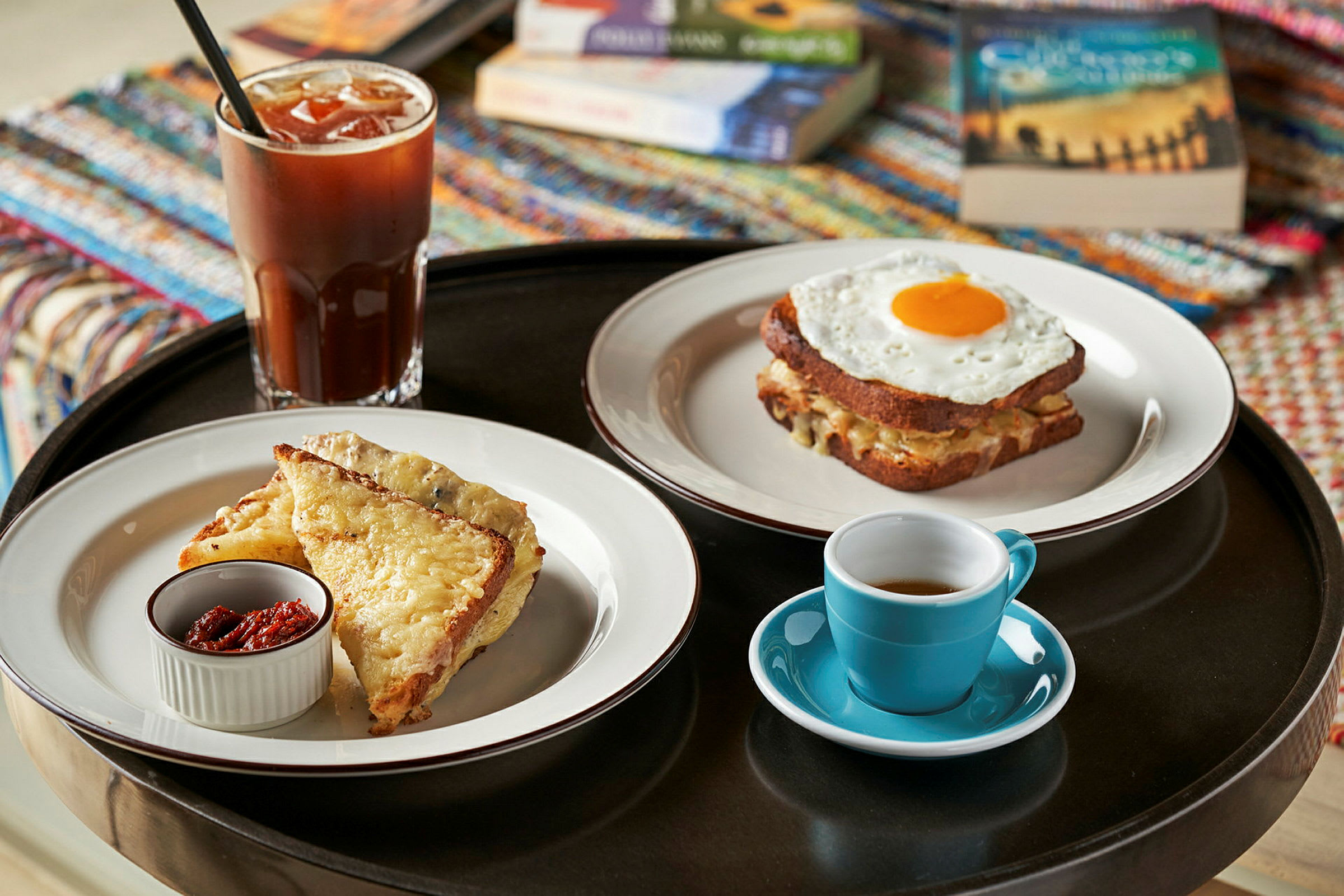 En bricka med en måltid bestående av bröd med ost och tillbehör, en kopp kaffe och ett glas kall dryck. (AI-genererad text)