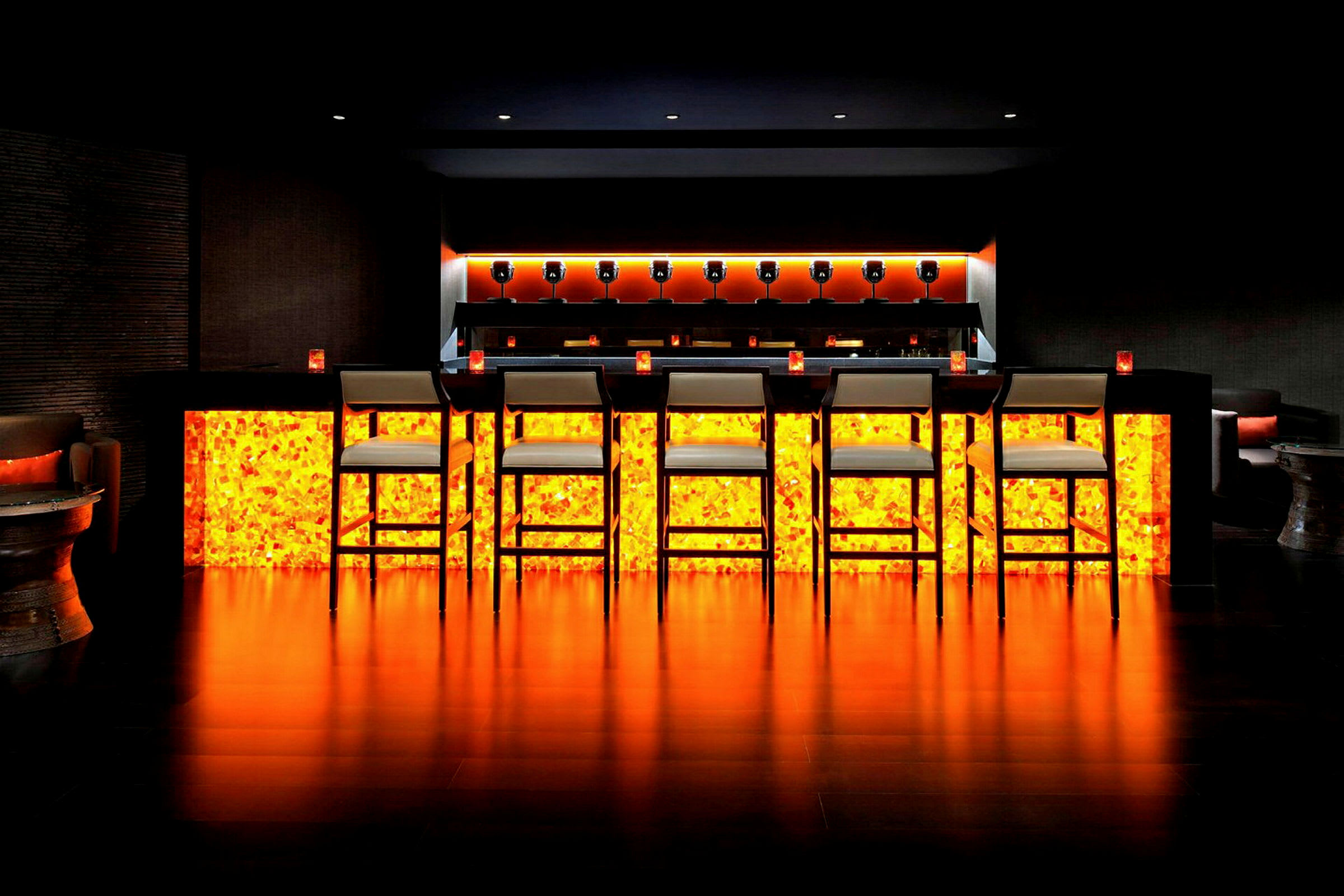 En bar med upplyst orange undertill, höga stolar och en modern inredning. (AI-genererad text)