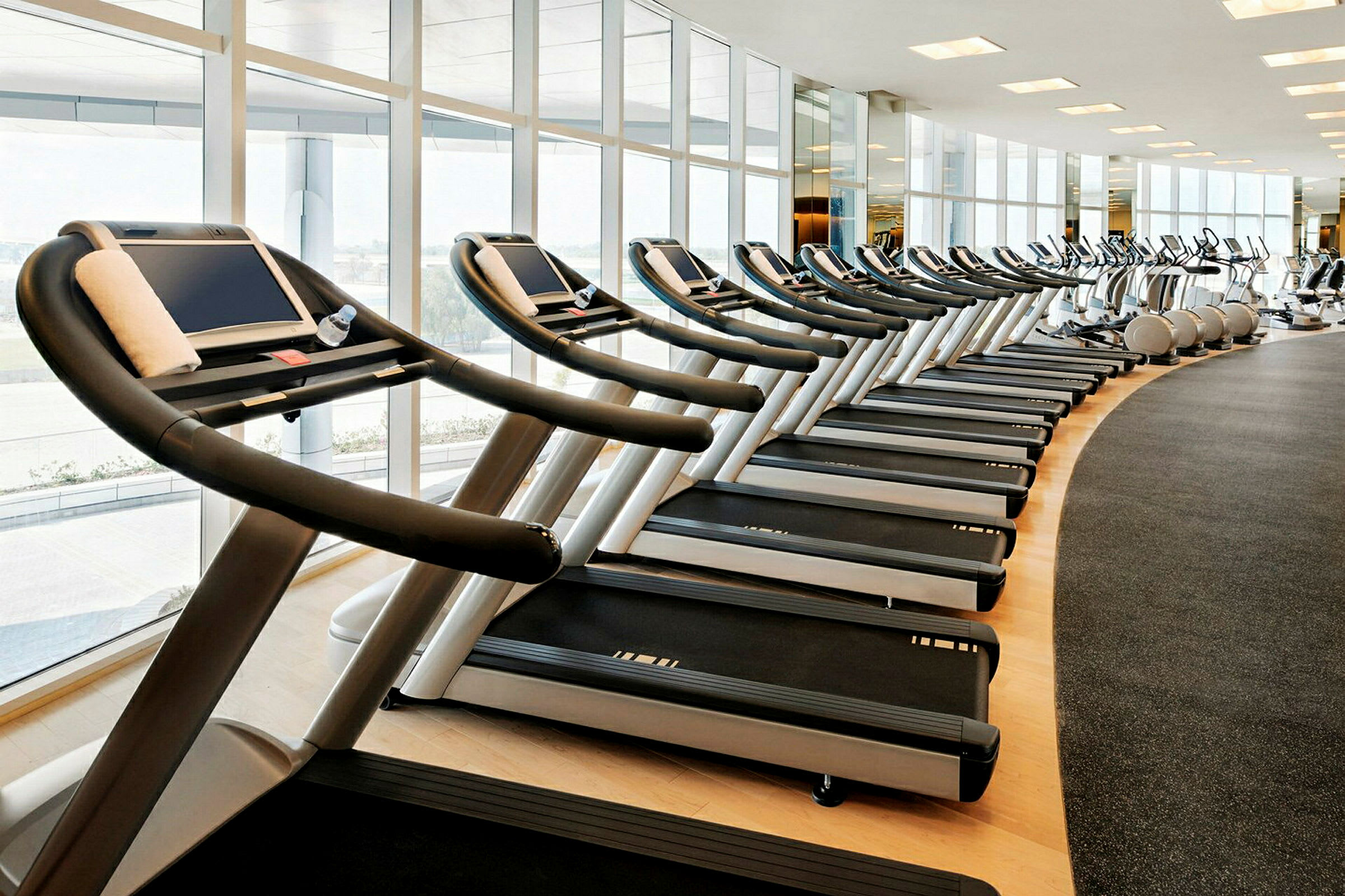 En rad av löpband i ett gym med stora fönster. (AI-genererad text)
