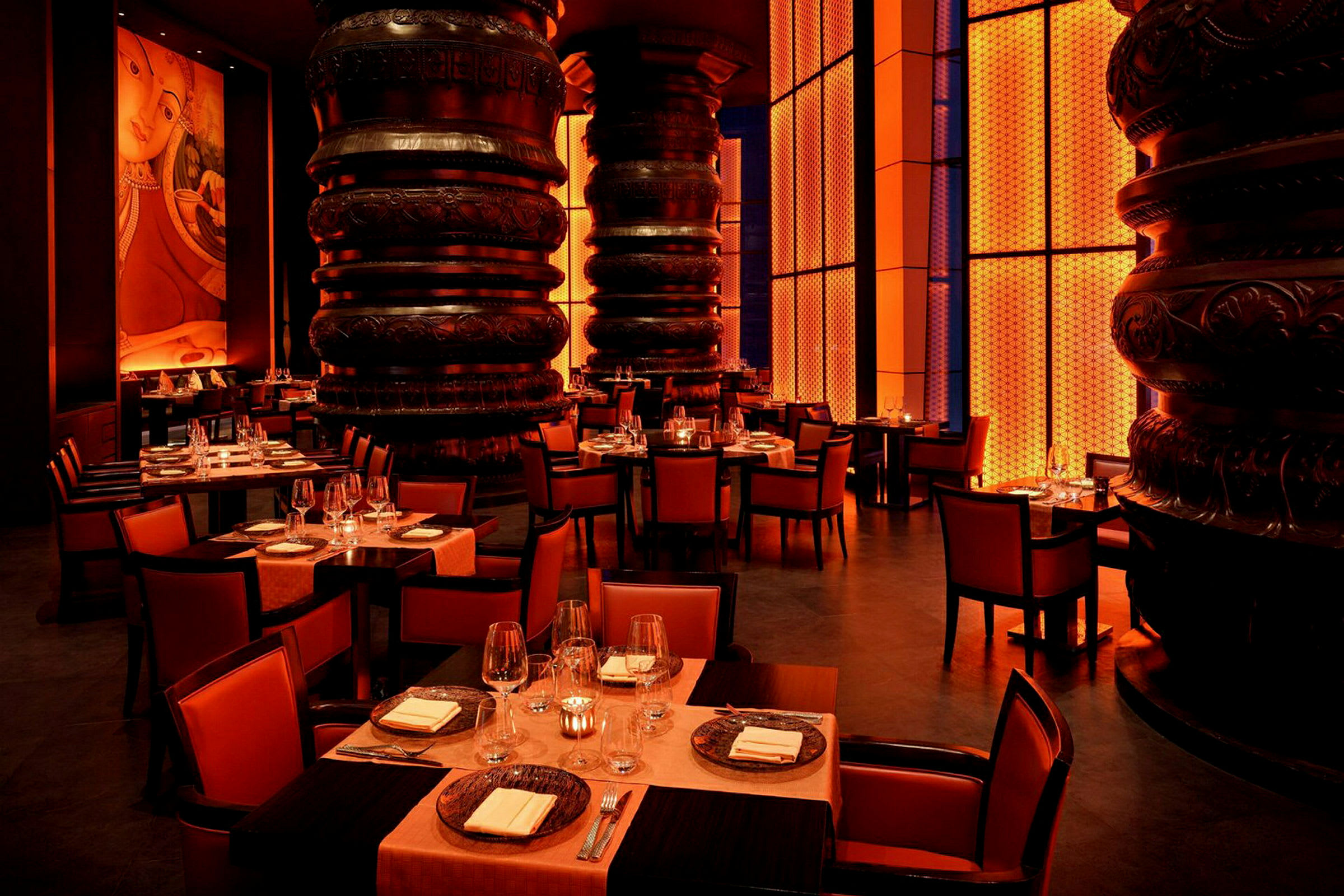 Interiör av en elegant restaurang med orange belysning, dekorerade pelare och dukade bord. (AI-genererad text)