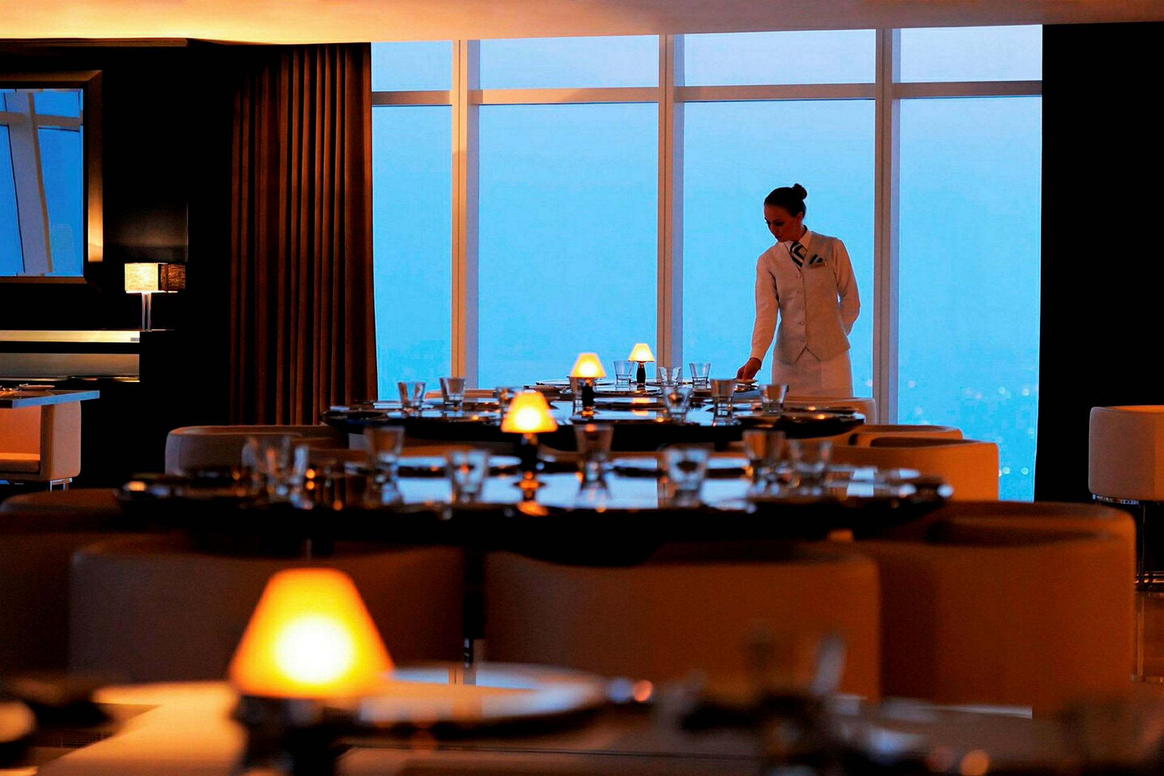 En restaurang med elegant dukade bord och stora fönster som vetter mot en utsikt. (AI-genererad text)