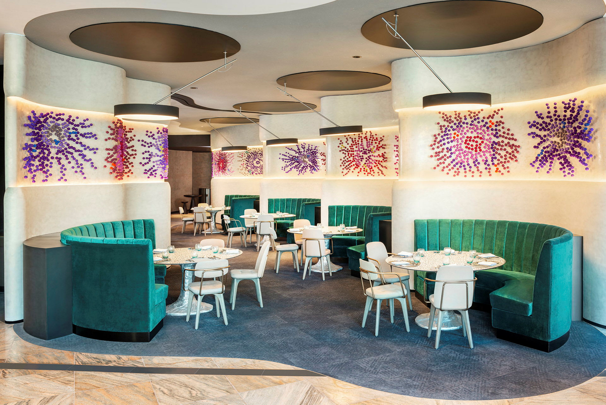 Ett modernt restaurangområde med gröna soffor och dekorativa väggkonstverk. (AI-genererad text)