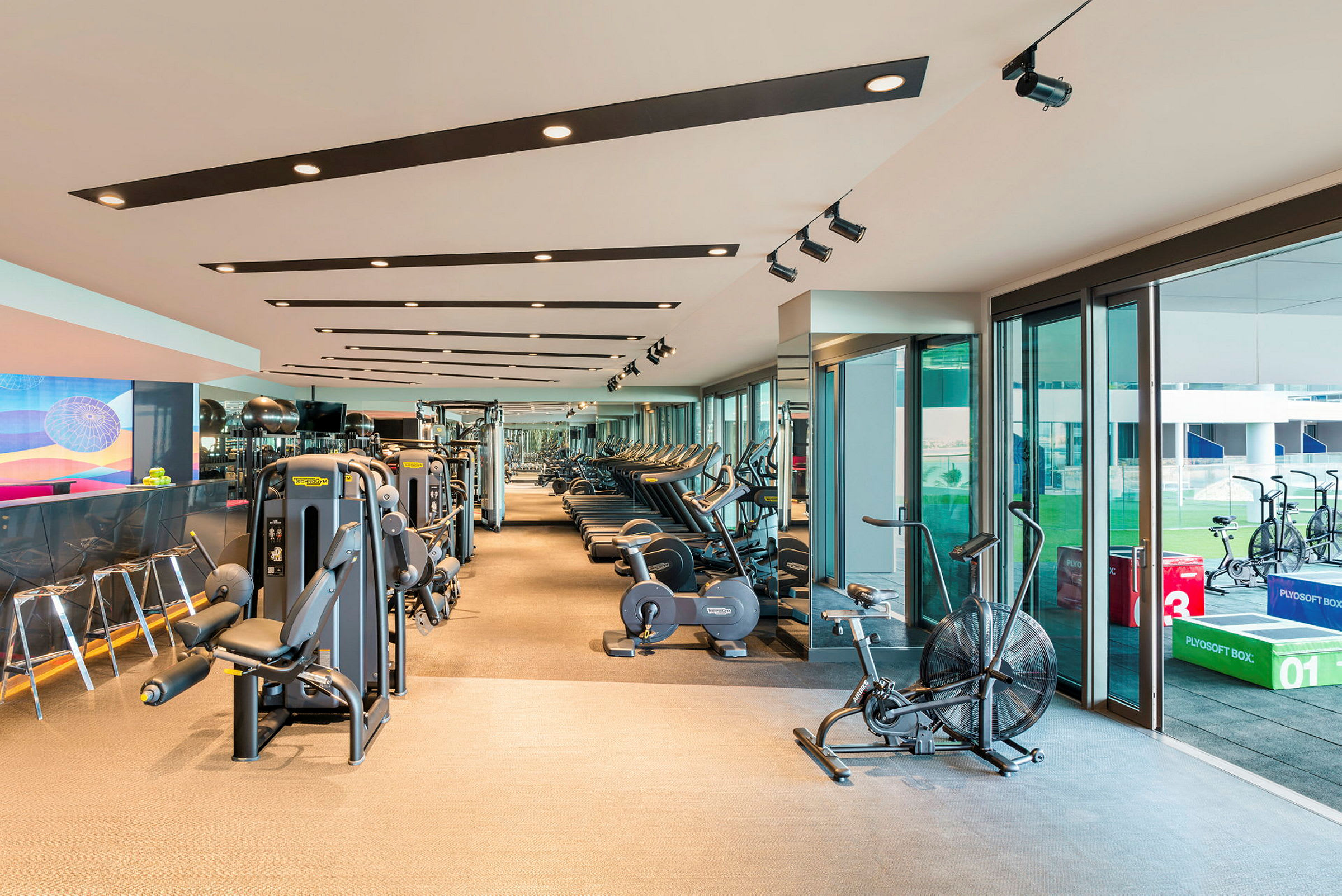 Ett modernt gym med träningsmaskiner och fönster som vetter mot en utomhusmiljö. (AI-genererad text)