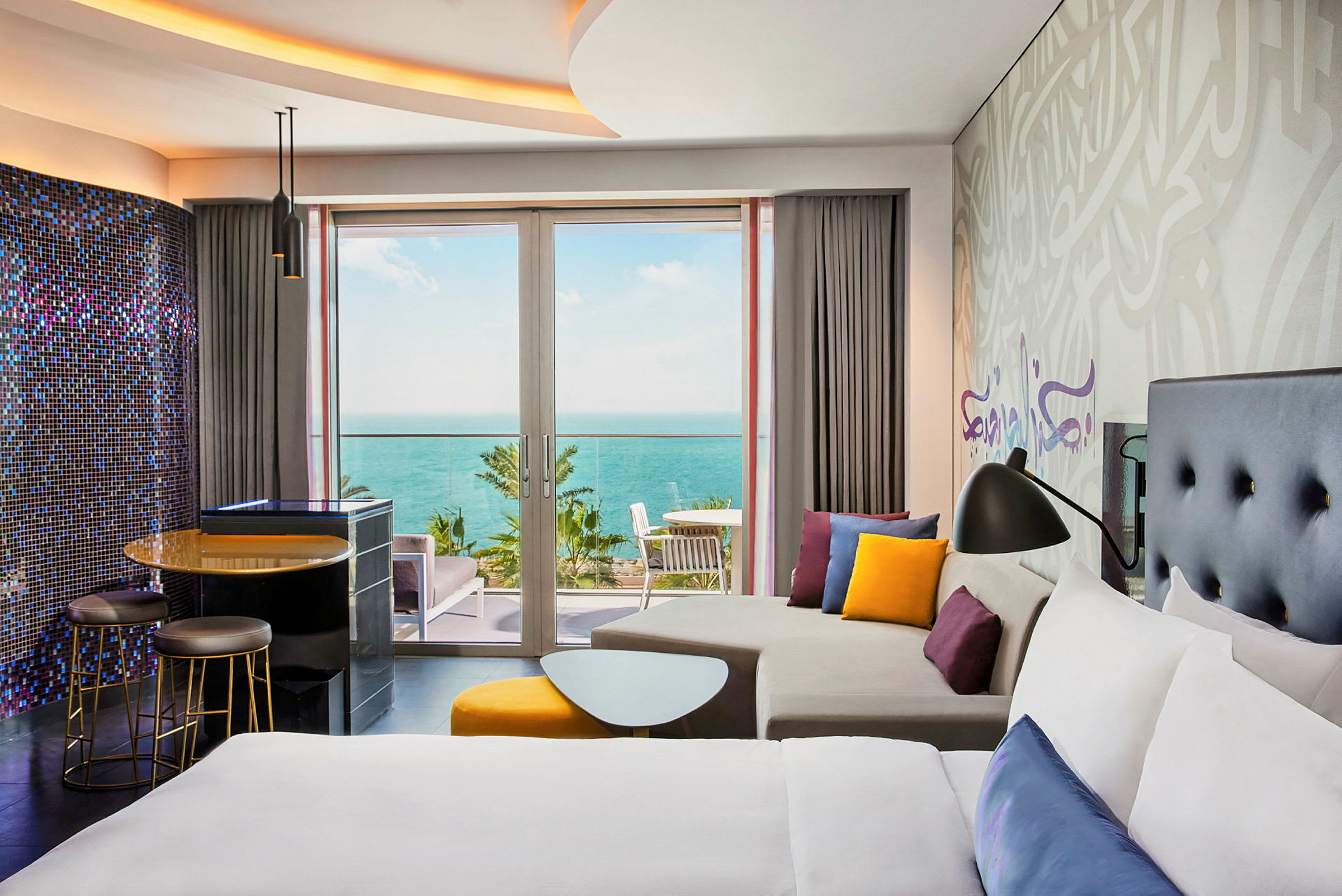 Hotellrum med modern inredning, säng och soffa samt utsikt över havet genom glasdörrar. (AI-genererad text)