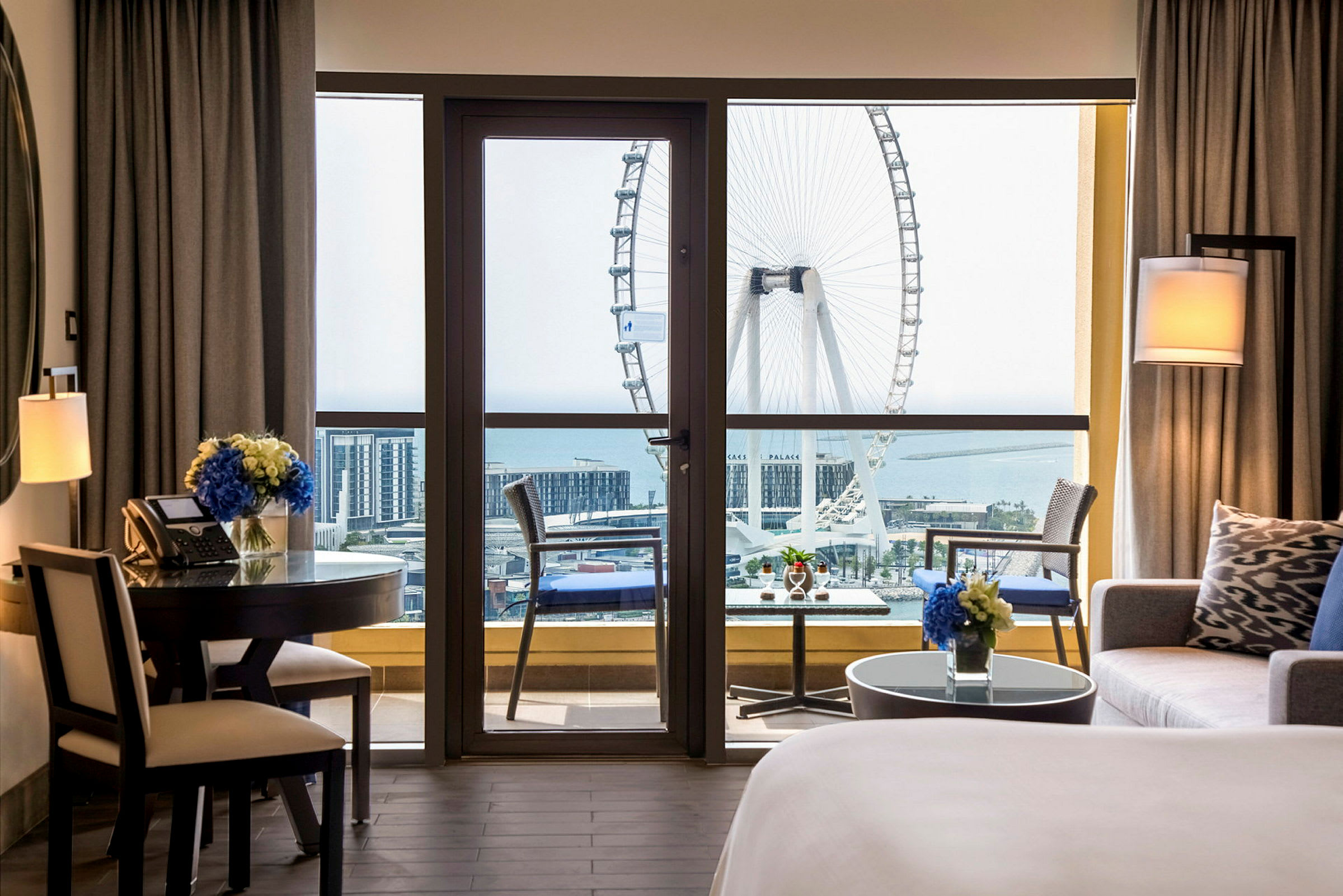 Ett hotellrum med en balkong som har utsikt över ett stort pariserhjul och havet. (AI-genererad text)
