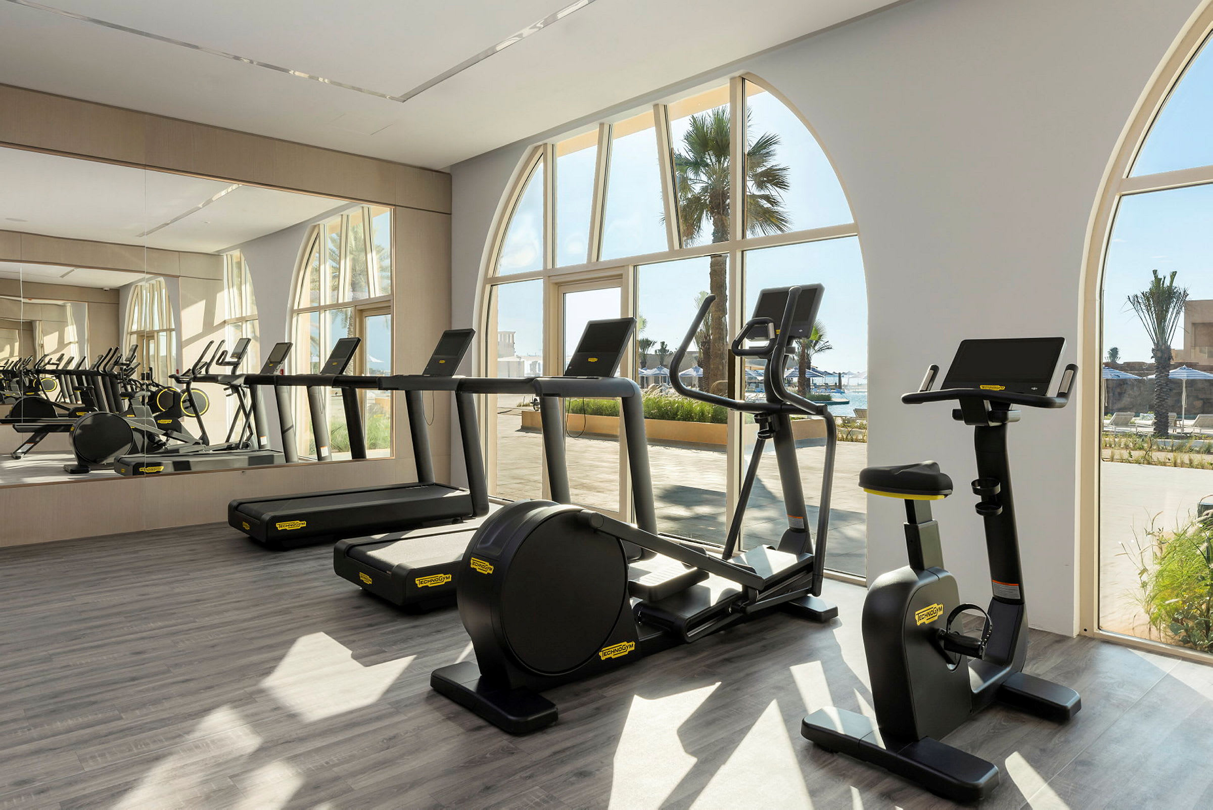 Träningsmaskiner i ett gym med fönster som vetter mot utomhusområdet. (AI-genererad text)