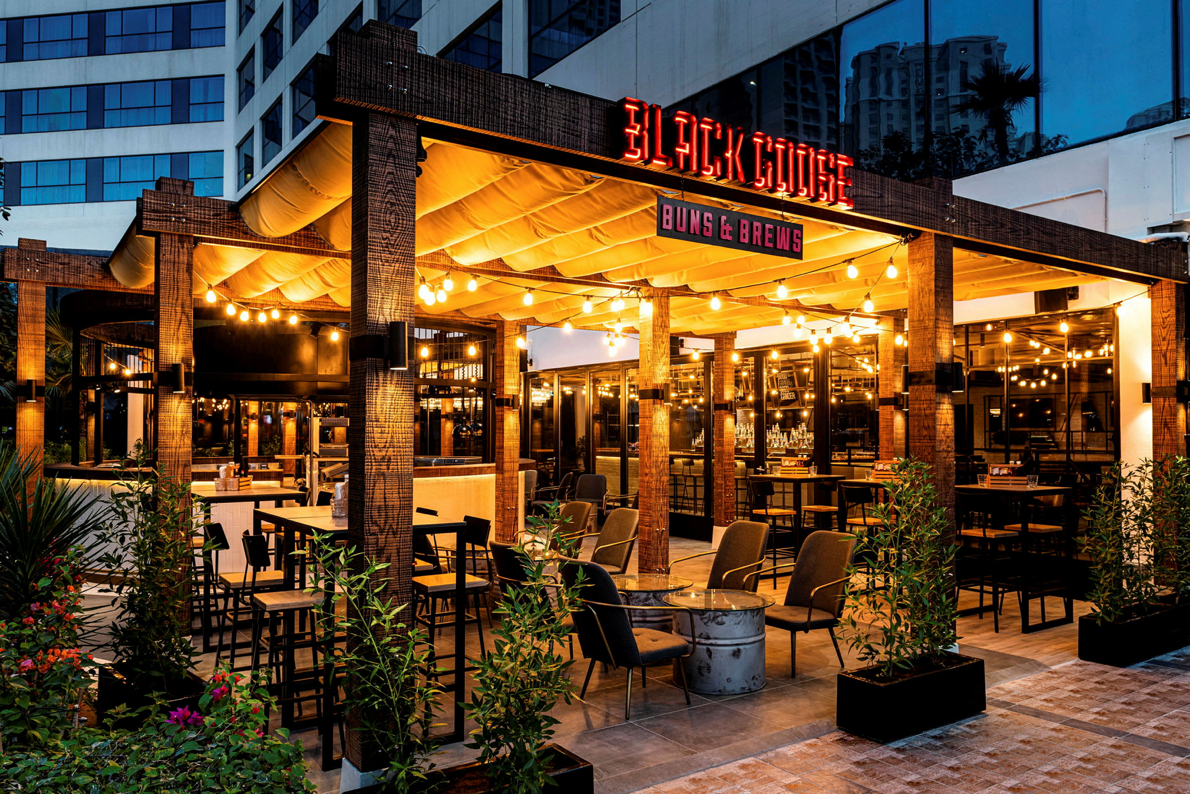 Bild av en utomhusrestaurang med namnet 'Black Goose', belyst och dekorativt med möbler och planteringar. (AI-genererad text)