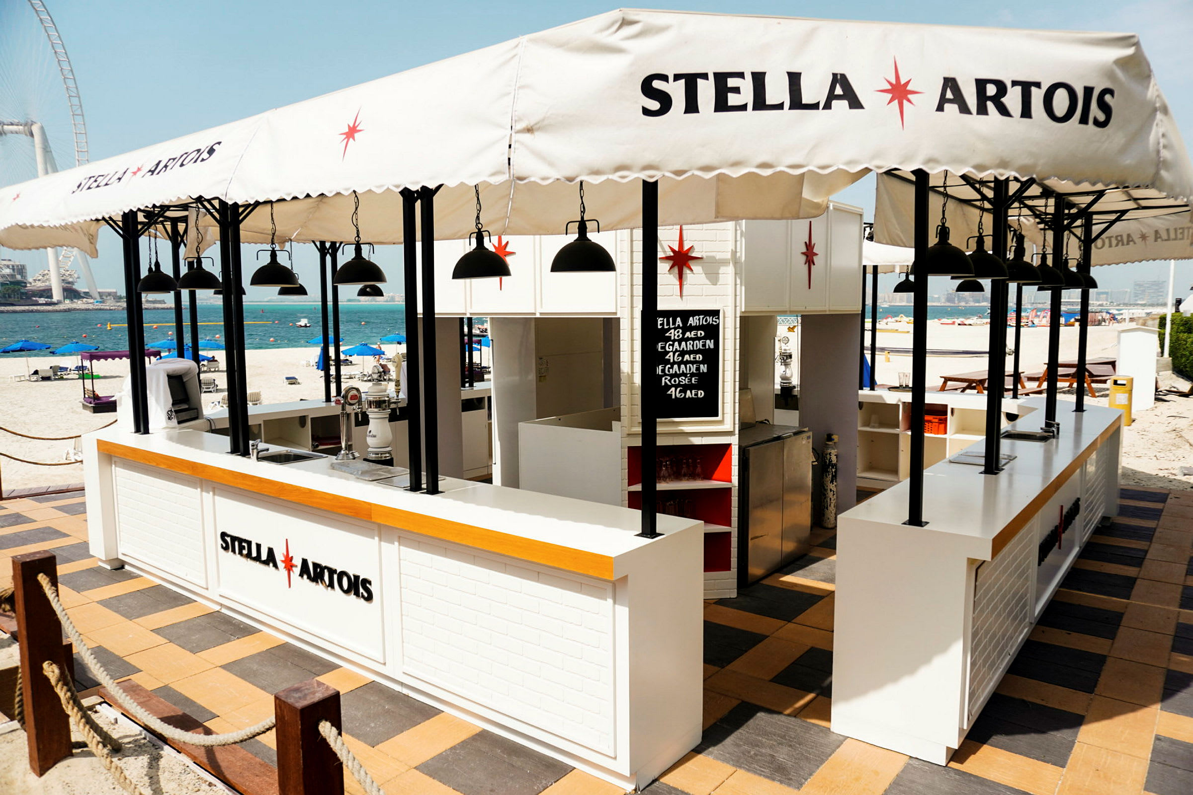 En strandbar med Stella Artois-logotyp, parasoller och bord. (AI-genererad text)