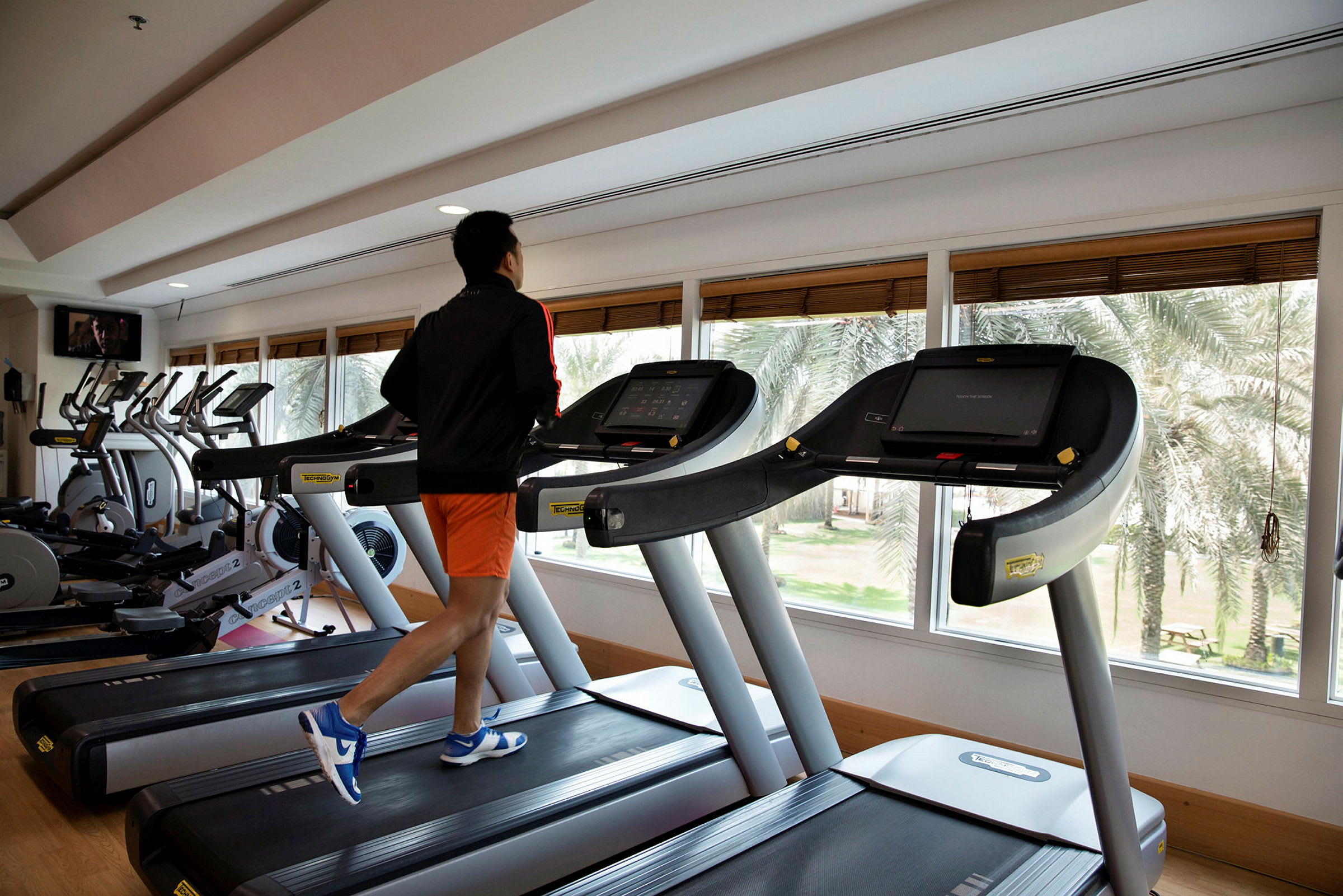Person springer på löpband i ett gym med stora fönster. (AI-genererad text)