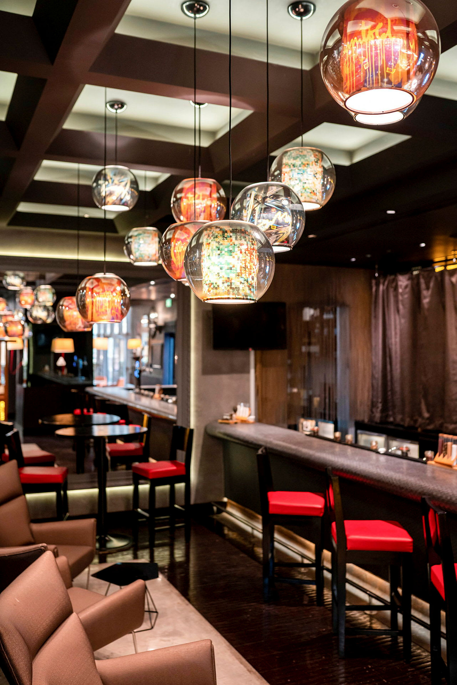 En bar med moderna möbler, röda stolar och hängande glaskupor som belysning. (AI-genererad text)