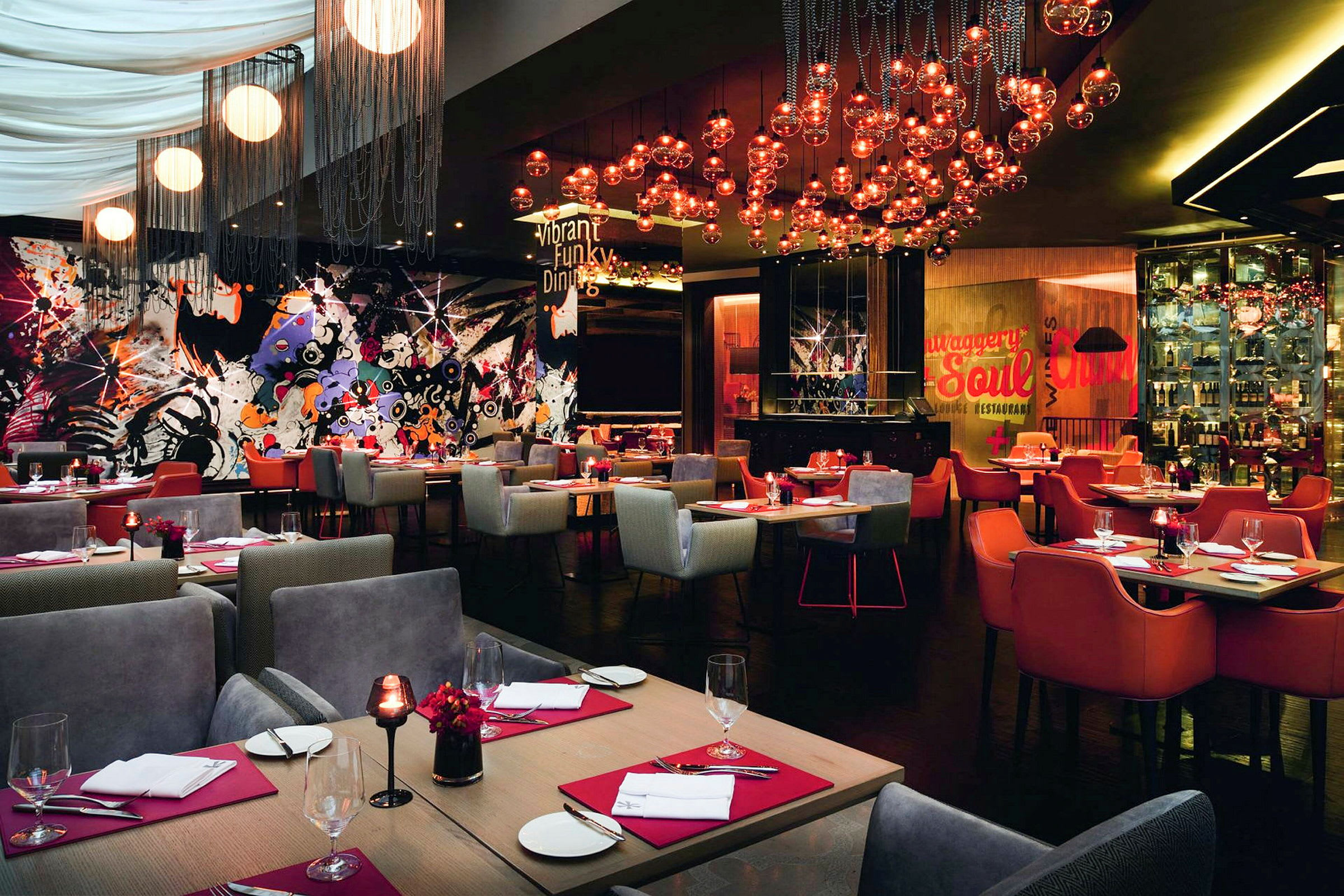 Restaurang med färgglad och modern inredning, bord med röda servetter och glas samt lampor hängande från taket. (AI-genererad text)