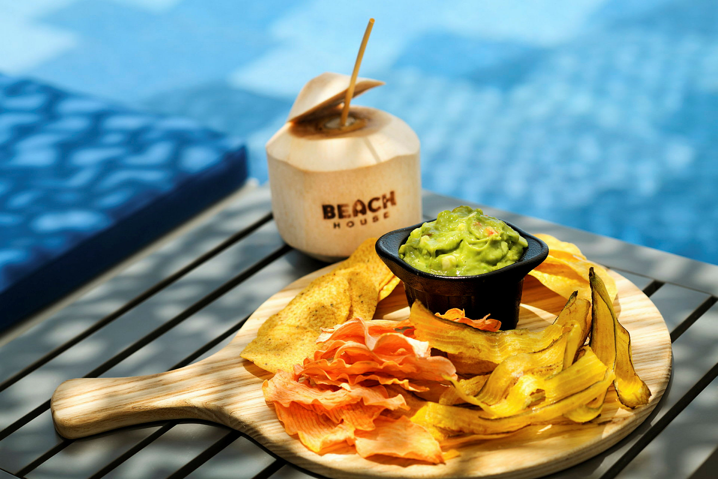 En tallrik med olika chips och guacamole samt en kokosnöt med texten 'Beach House'. (AI-genererad text)