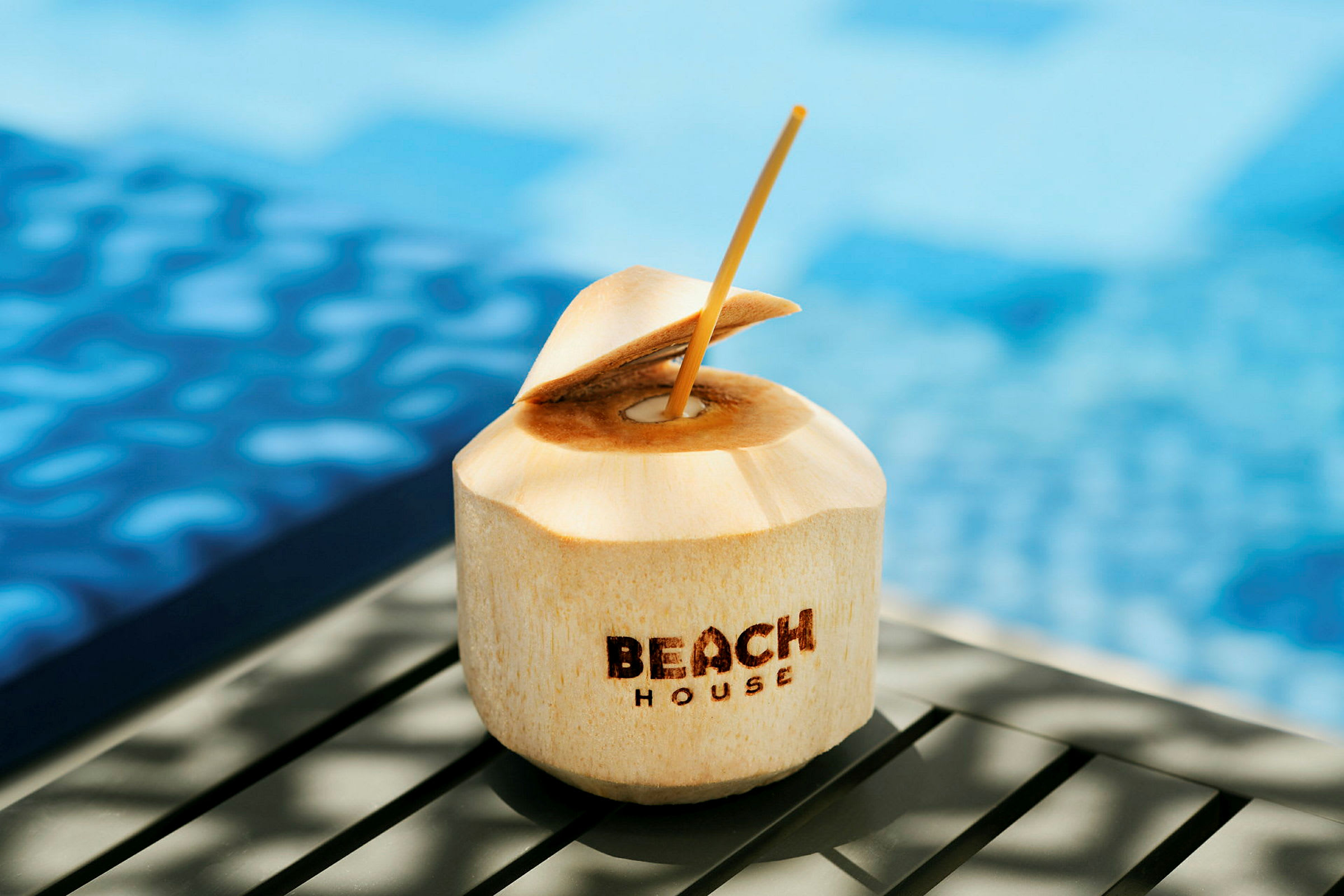En kokosnöt med texten 'Beach House' placerad nära en pool. (AI-genererad text)