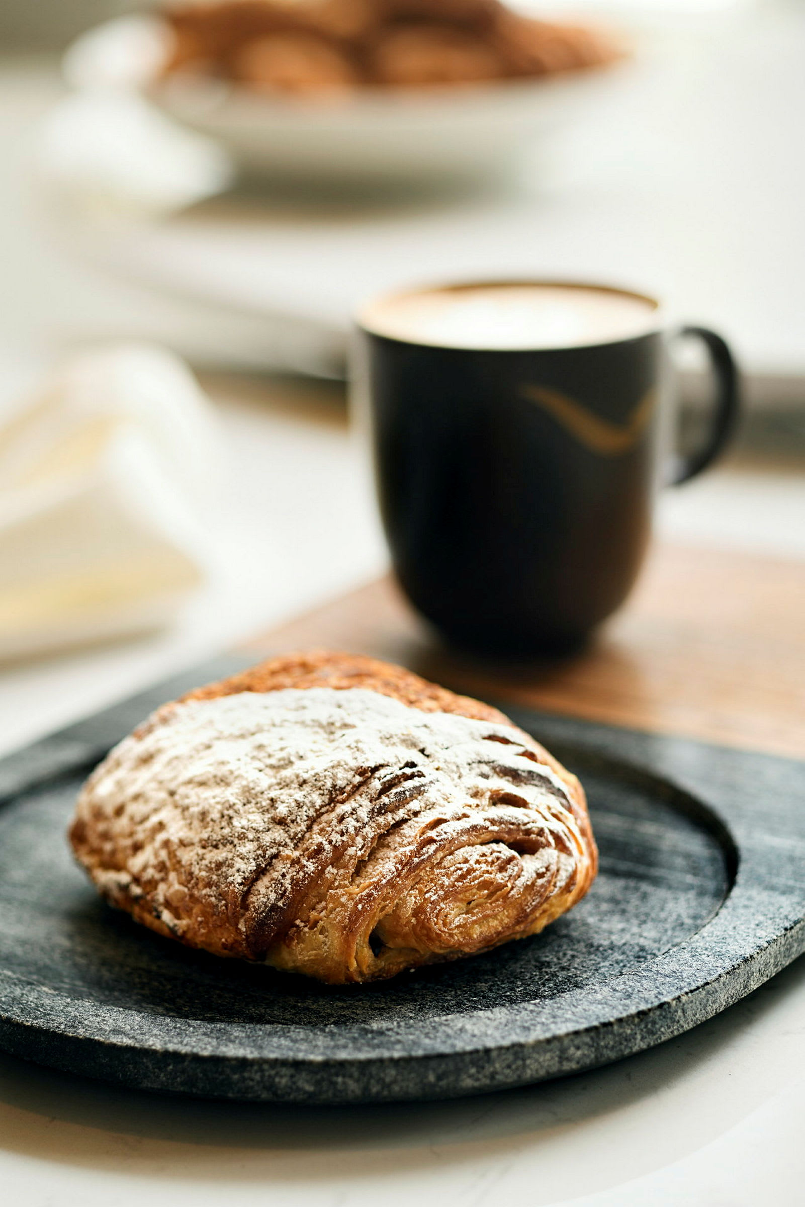 En kopp kaffe och en bulle med florsocker på ett fat. (AI-genererad text)