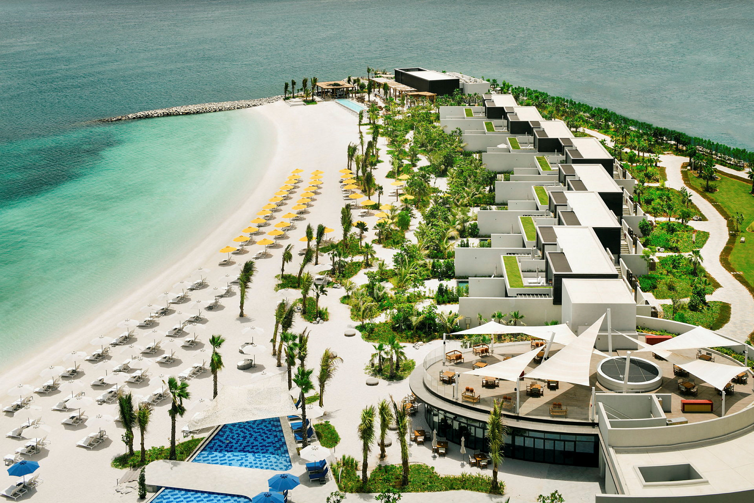 Flygfoto över strand med solstolar och parasoller framför hotellområde med grönska. (AI-genererad text)
