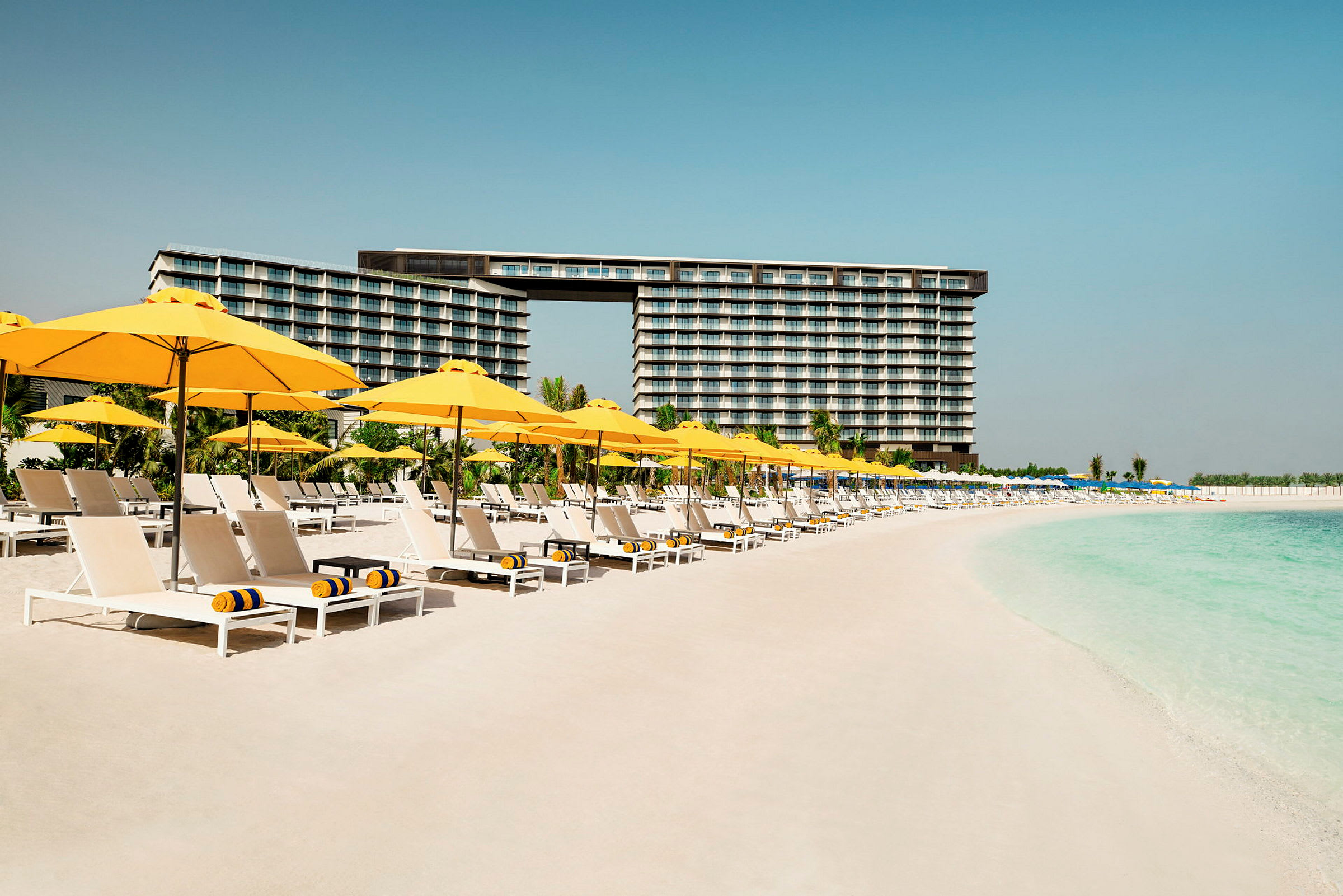 Strand med solstolar och parasoller framför ett hotell. (AI-genererad text)