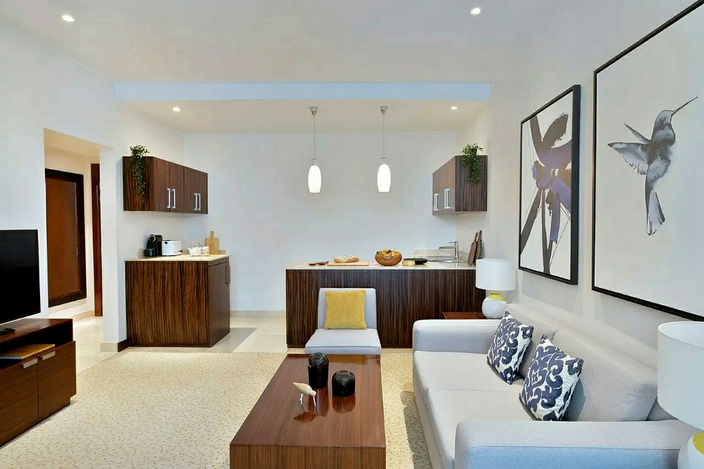 Ett vardagsrum med en soffa, ett soffbord, en TV och ett kök i bakgrunden. (AI-genererad text)