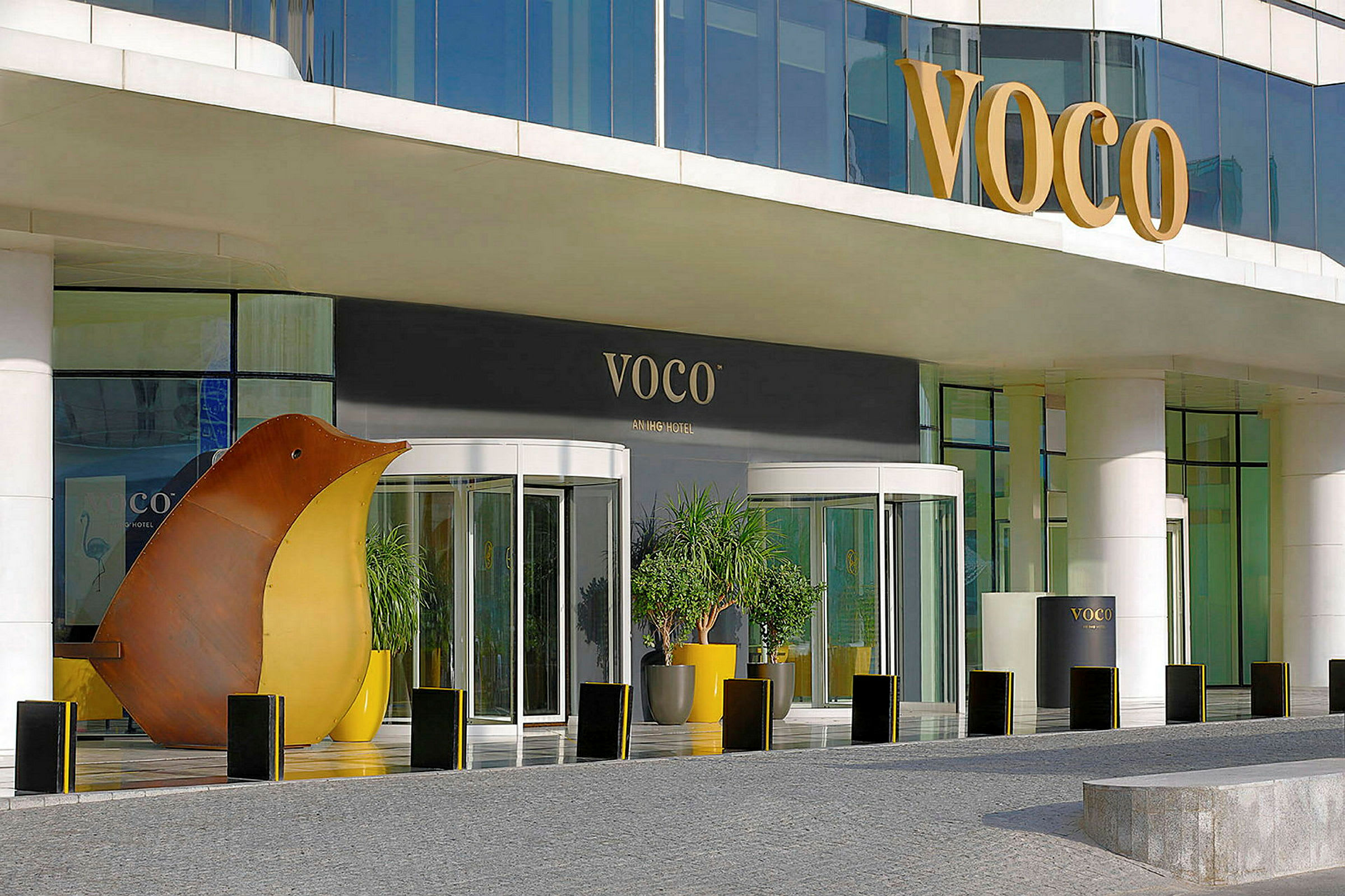 Entré till ett hotell med glasdörrar och skylt med texten 'VOCO', samt dekorationer och växter. (AI-genererad text)