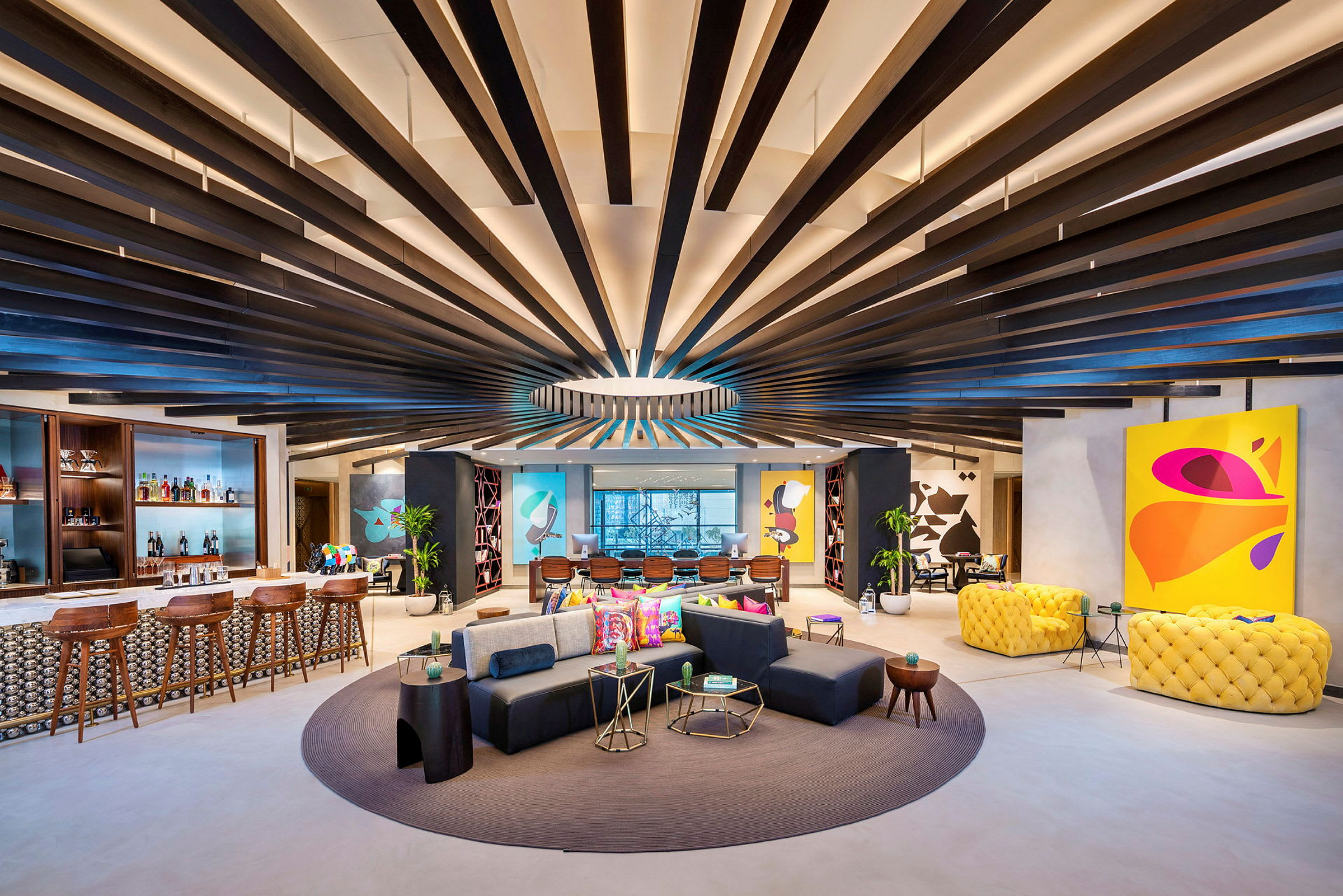 Moderna och färgglada möbler i en rymlig lounge med ett designat tak och konst på väggarna. (AI-genererad text)