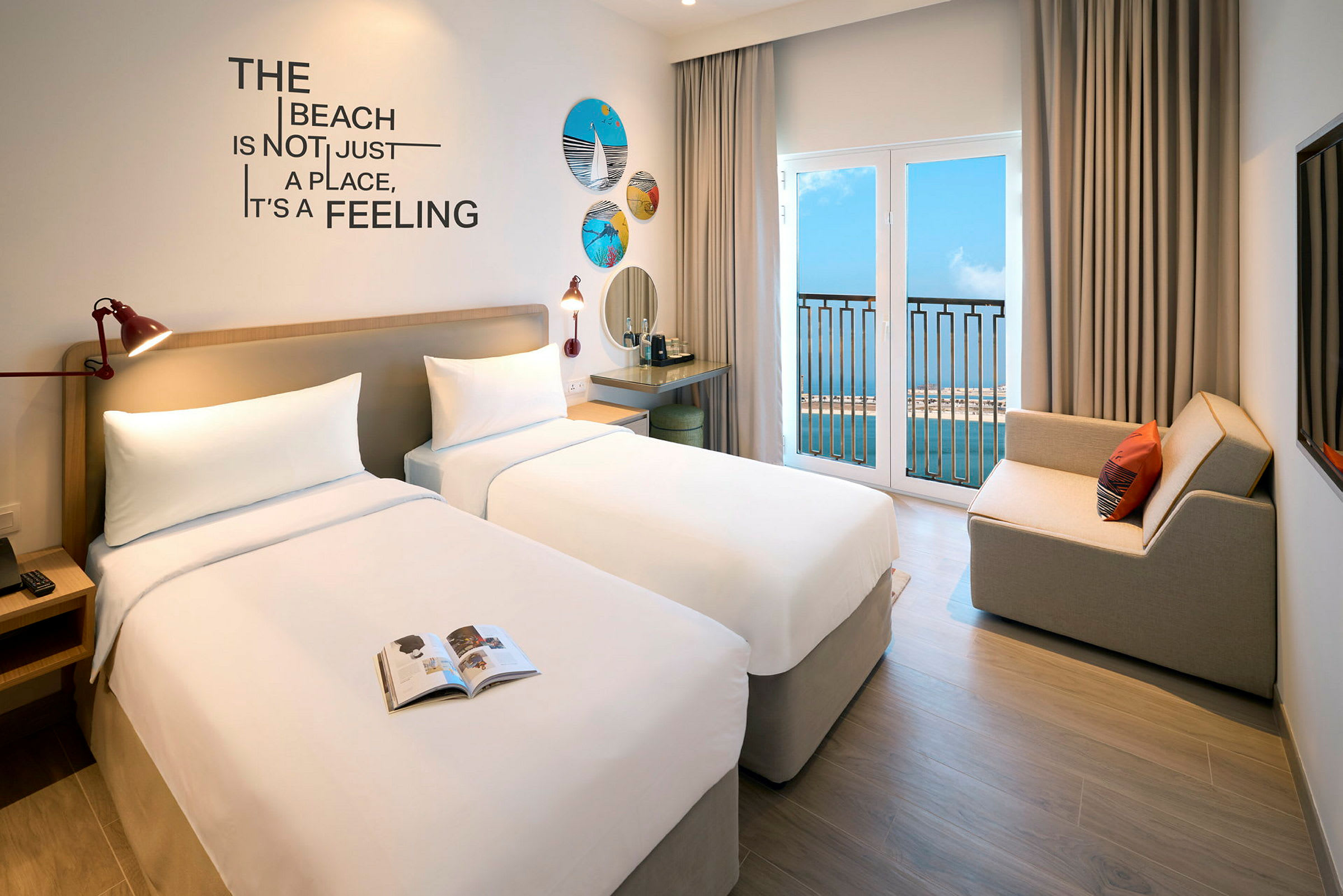 Hotellrum med två sängar, en soffa och havsutsikt genom altandörrar. (AI-genererad text)