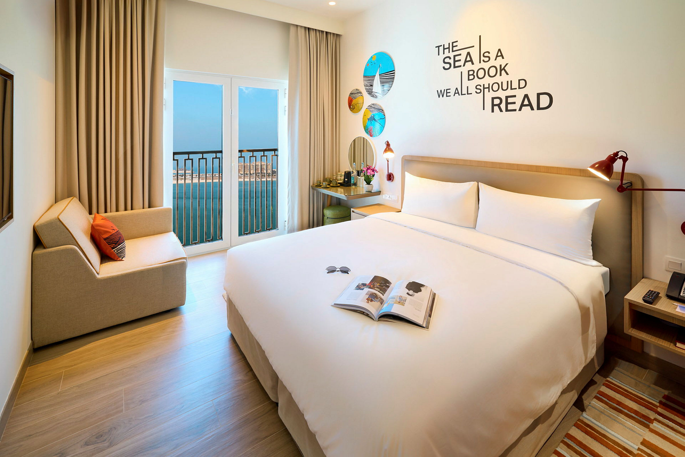 Ett hotellrum med en stor säng, sittplats, och öppet fönster med utsikt över havet. (AI-genererad text)