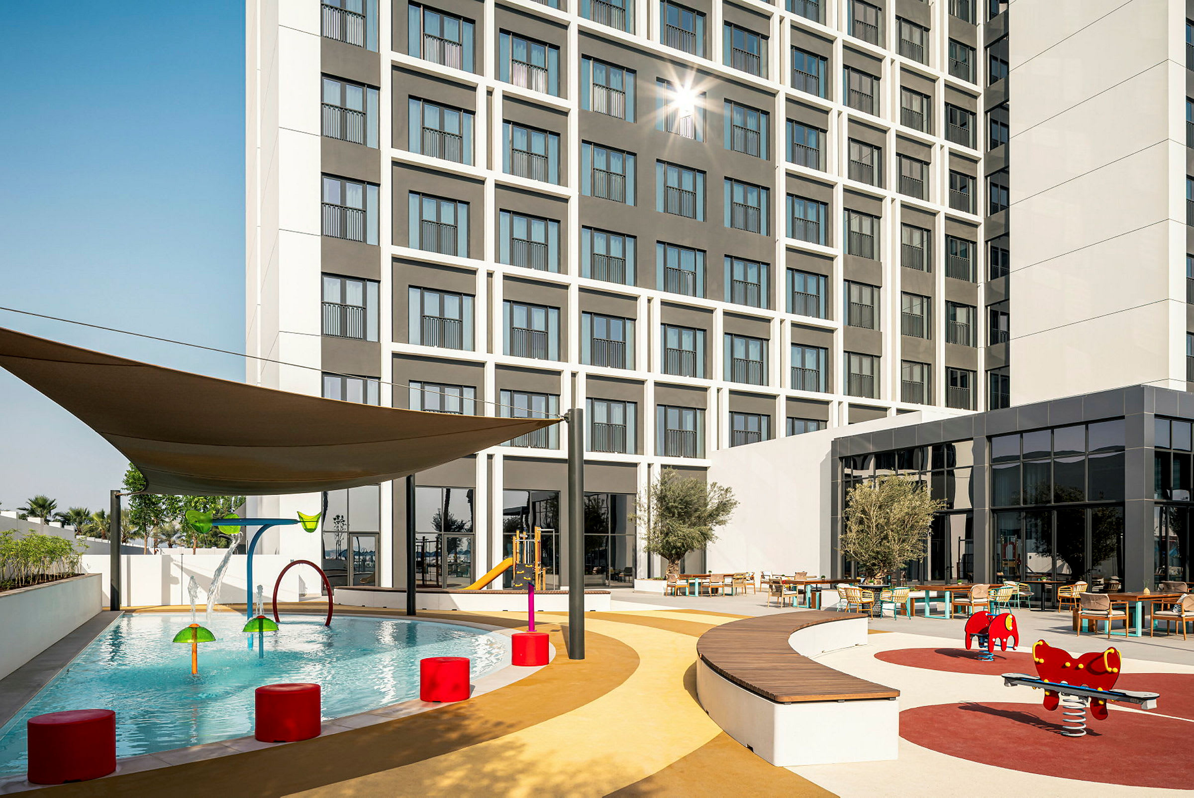Utomhus område med barnpool, lekplats och sittplatser framför ett hotell. (AI-genererad text)