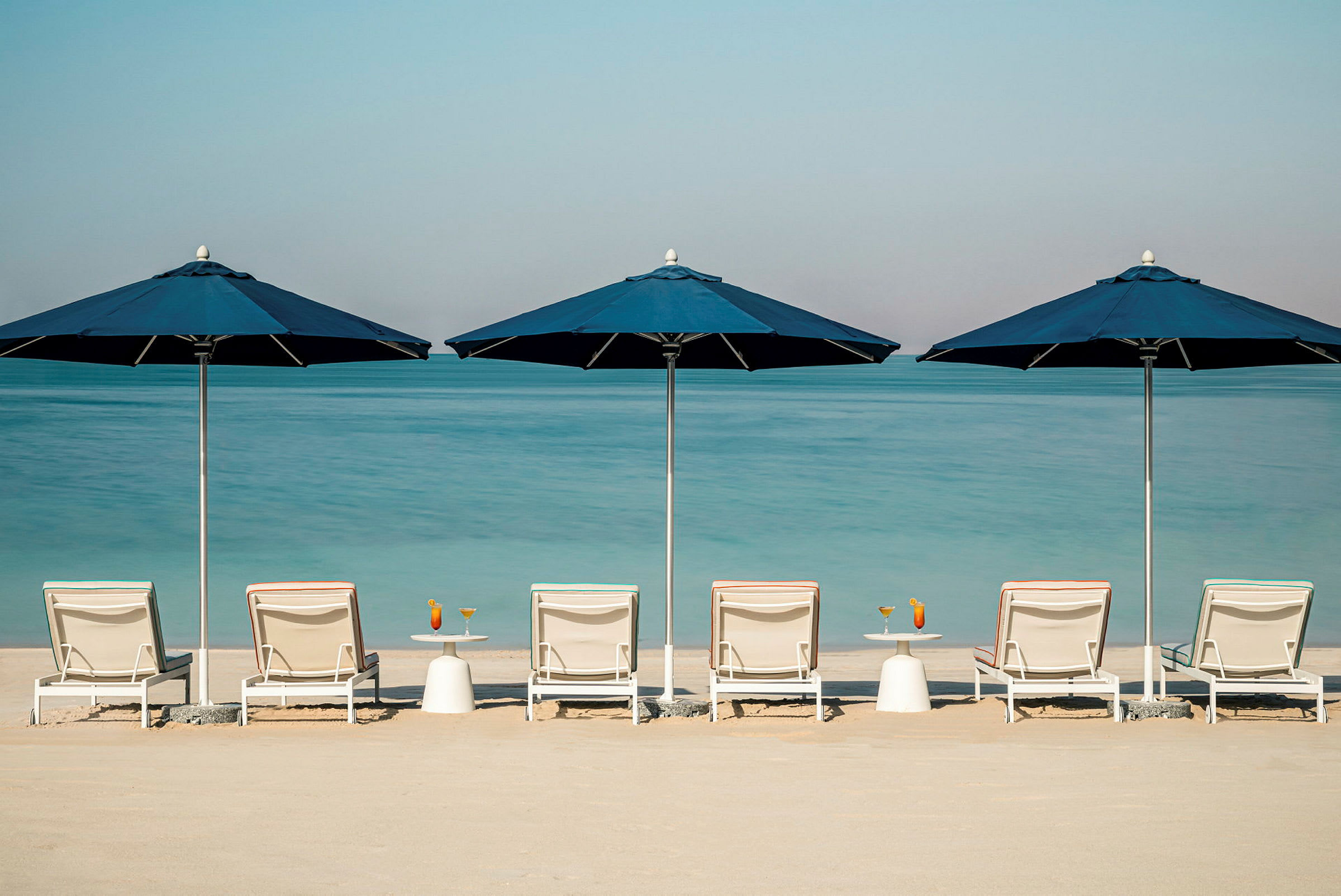Strand med solstolar och blå parasoller framför havet. (AI-genererad text)