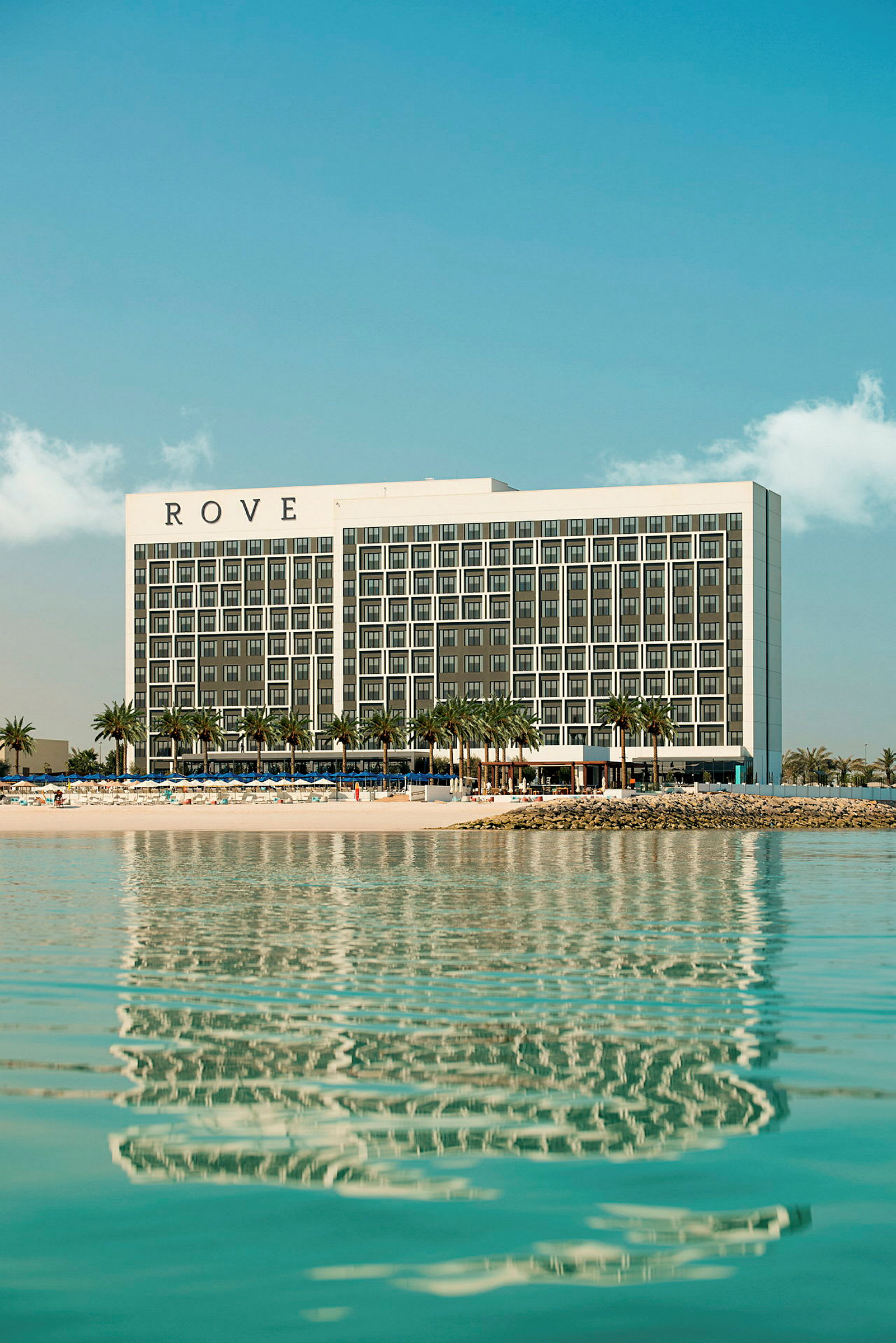 Hotellet Rove vid strand med palmer och vatten. (AI-genererad text)