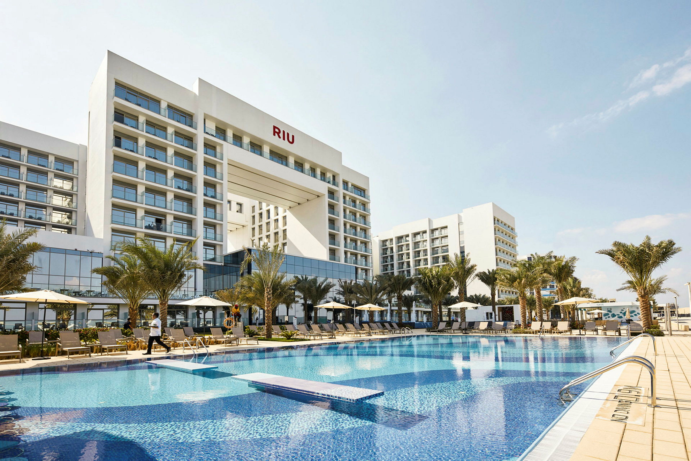 Hotellbyggnad med pool och solstolar framifrån. (AI-genererad text)