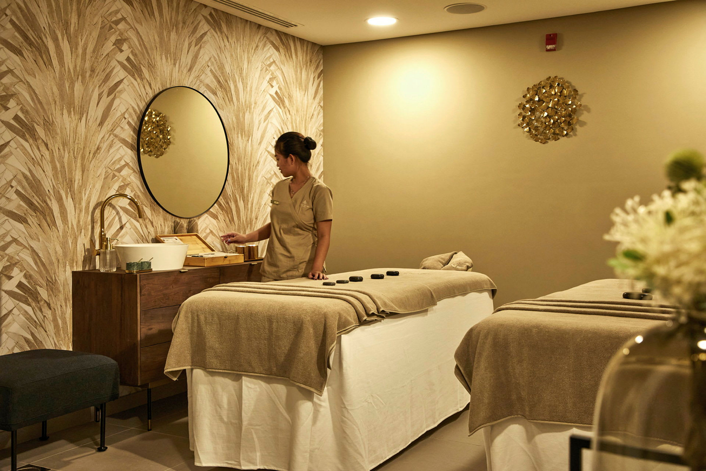 Ett behandlingsrum med två massagebänkar, neutralt inrett med beige och bruna toner. (AI-genererad text)