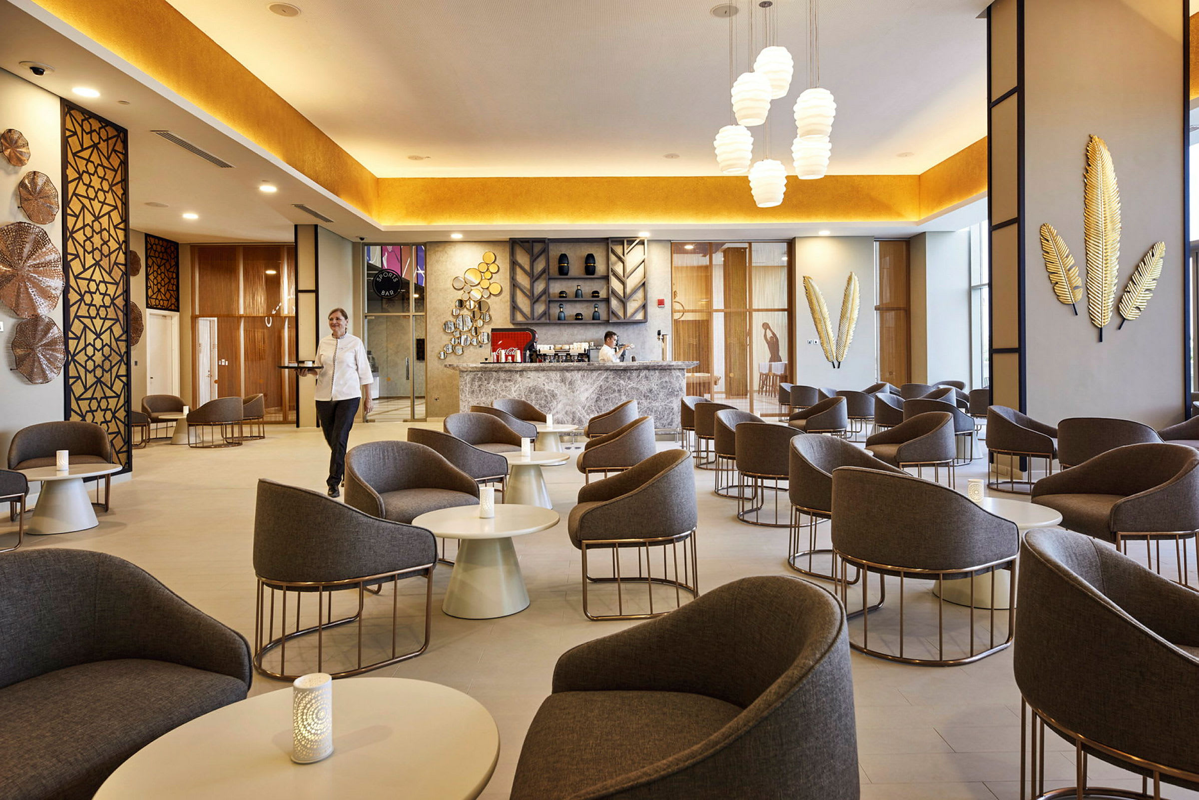 Ett modernt kafé/lounge med bekväma fåtöljer och bord, dekorativa väggdetaljer och en välkomnande bardisk. (AI-genererad text)