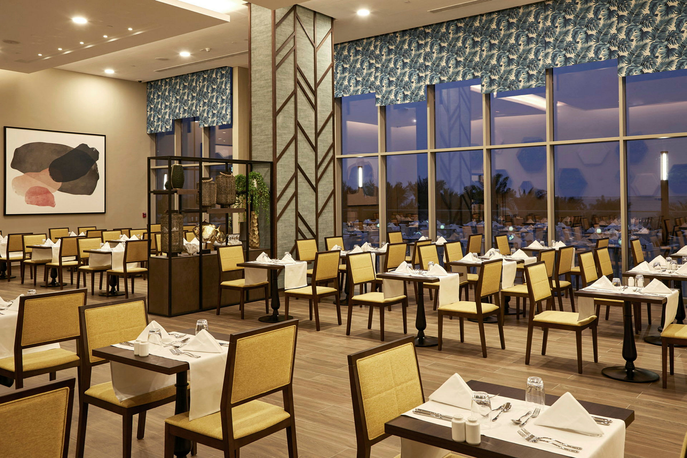 En restaurang interiör med dukade bord och stolar, belägen i en modern miljö med stora fönster som ger utsikt mot utsidan. (AI-genererad text)