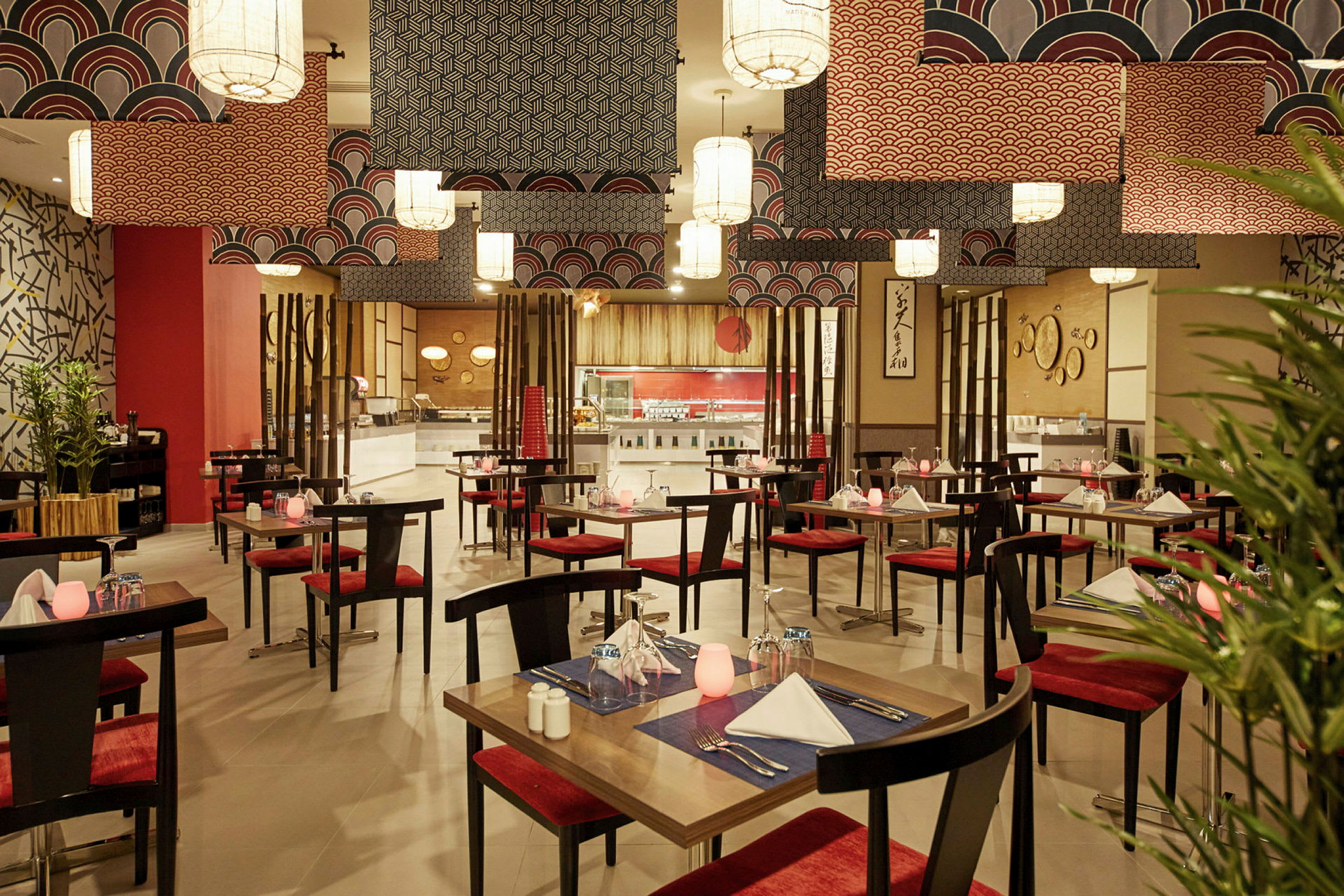En restaurang med bord och röda stolar, dekorerad med orientaliska motiv och moderna taklampor. (AI-genererad text)