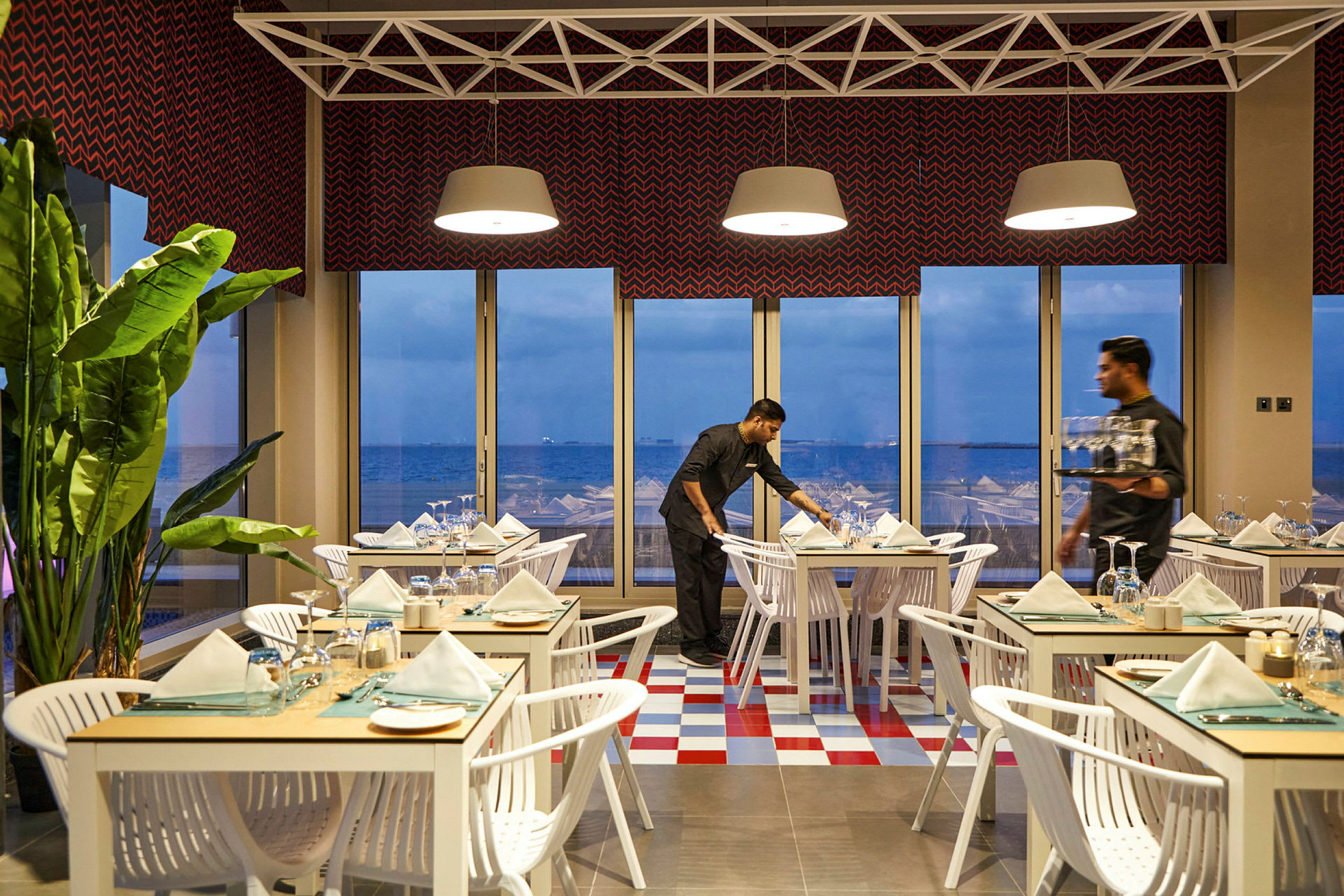 En ljus restaurang med dukade bord och en panoramavy över havet genom stora fönster. (AI-genererad text)