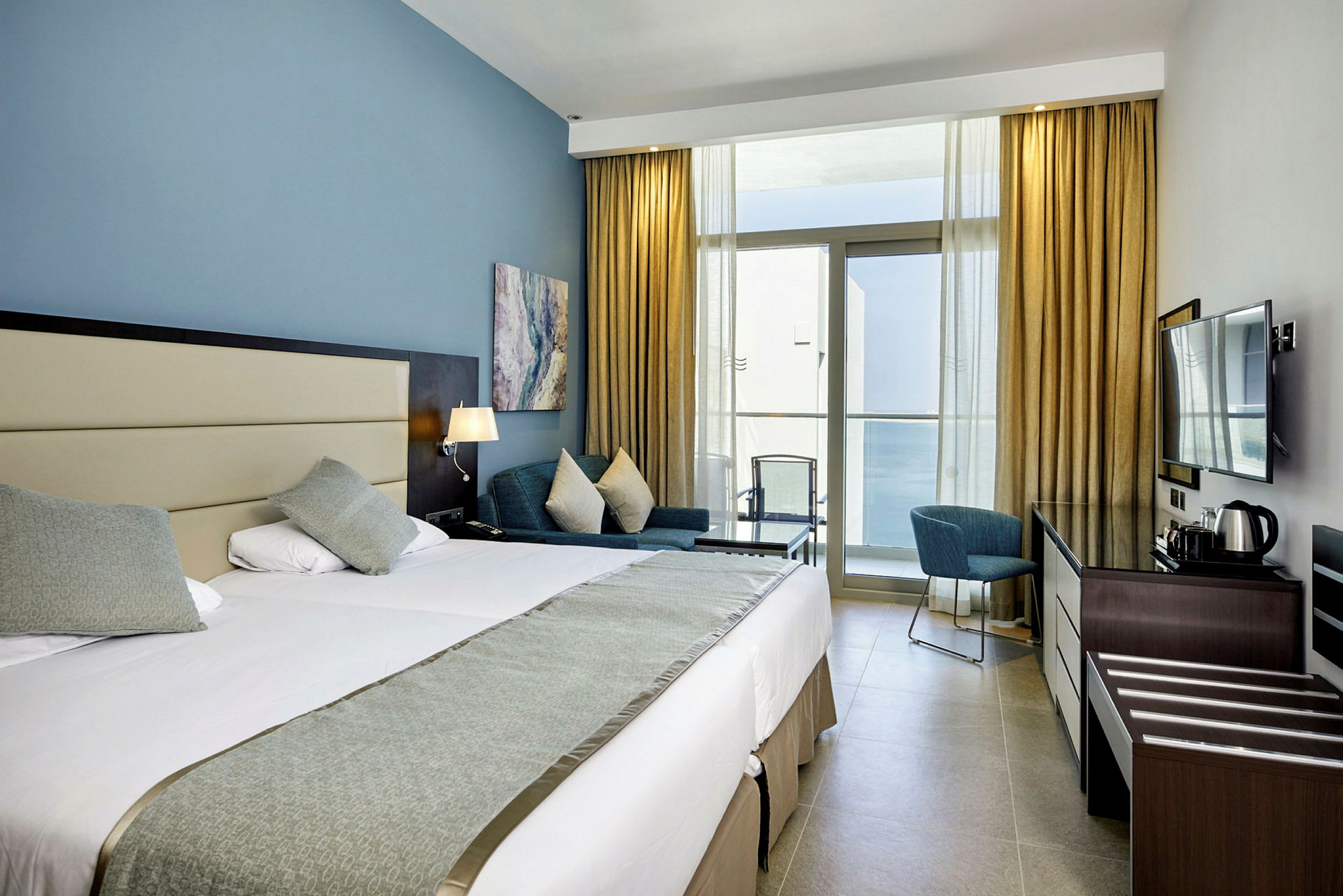 Hotellrum med dubbelsäng, fåtölj, och en balkongöppning (AI-genererad text)