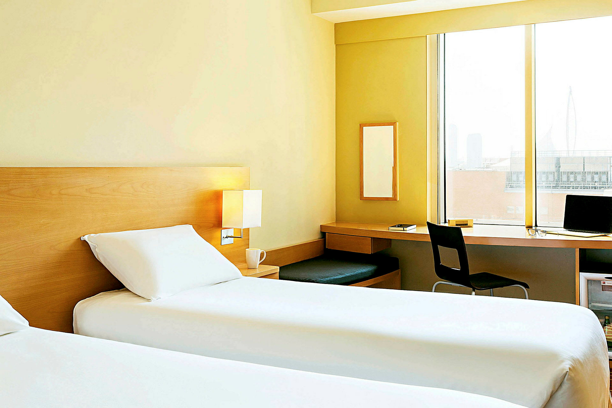 Ett hotellrum med två enkelsängar, ett skrivbord och en stor fönsteryta. (AI-genererad text)