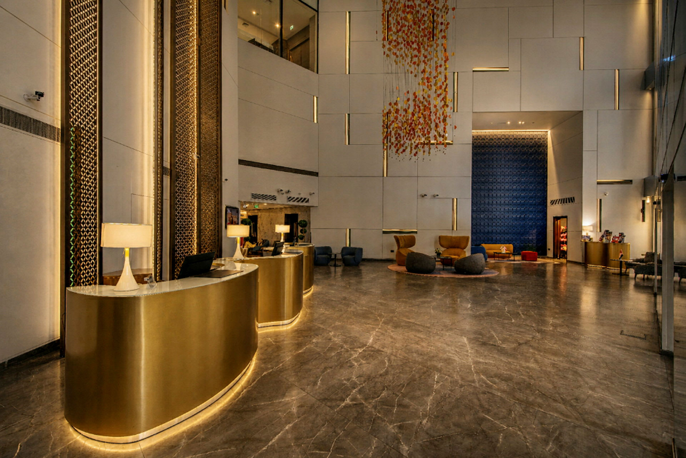En hotellobby med ett elegant marmorgolv, guldinredda receptioner och moderna sittmöbler. Ljusa väggar kompletteras med dekorativa detaljer och färgglada installationer. (AI-genererad text)