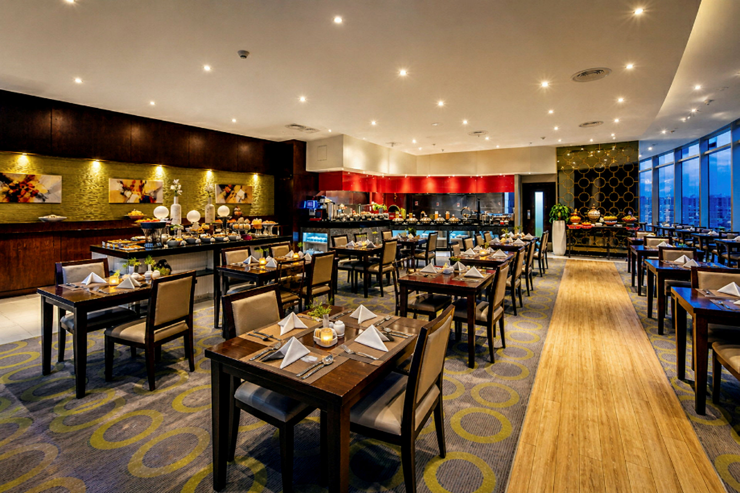 Ett elegant restaurangområde med mörka trämöbler och bord dekorerade med servetter och bestick. Buffé stationer i bakgrunden. (AI-genererad text)